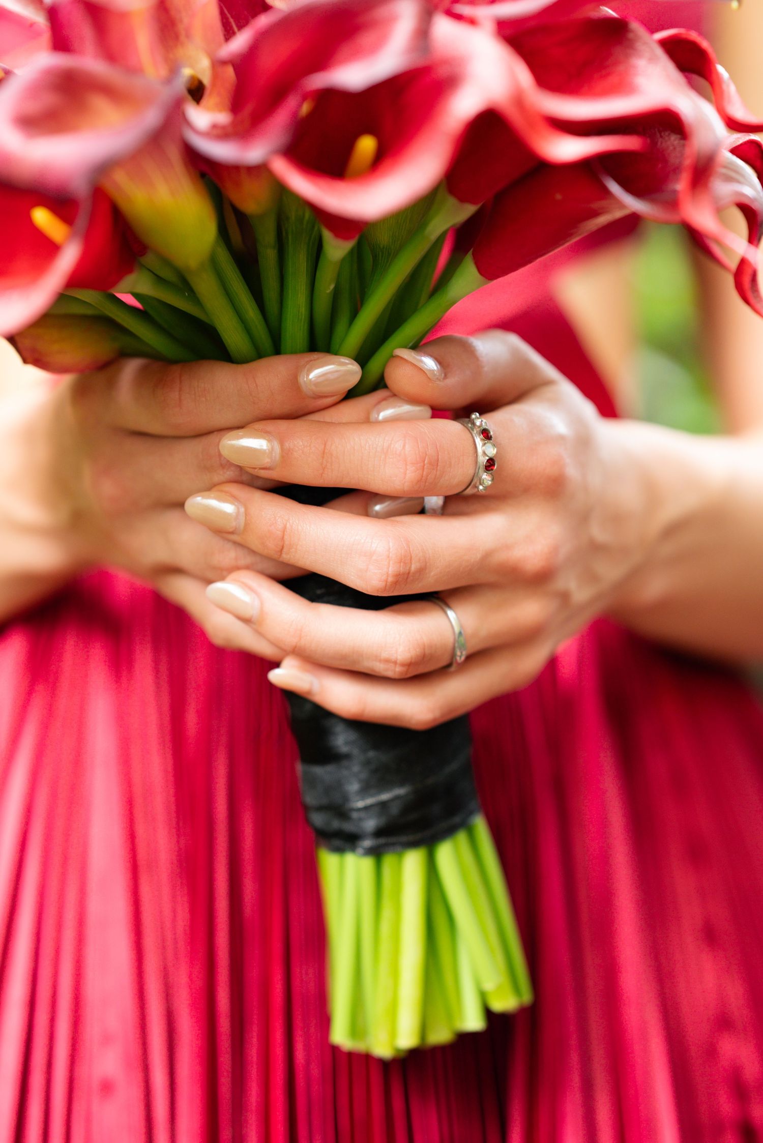 Hands holding pink calla lily bouquet against red formal dress.