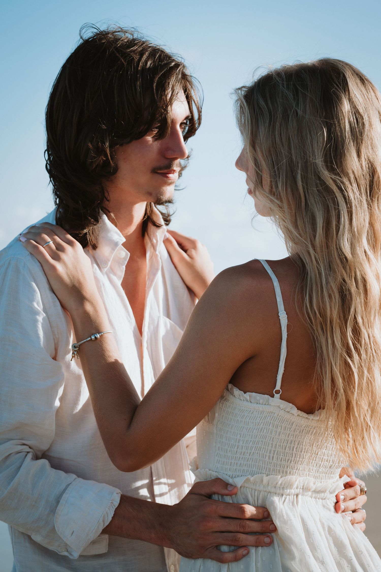 Romantic beach photos of couple in white outfits sharing intimate moments.