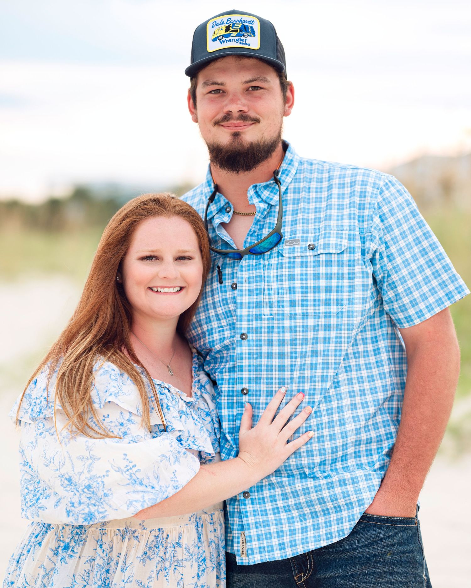 A couple poses together on the beach wearing coordinating blue and white outfits.