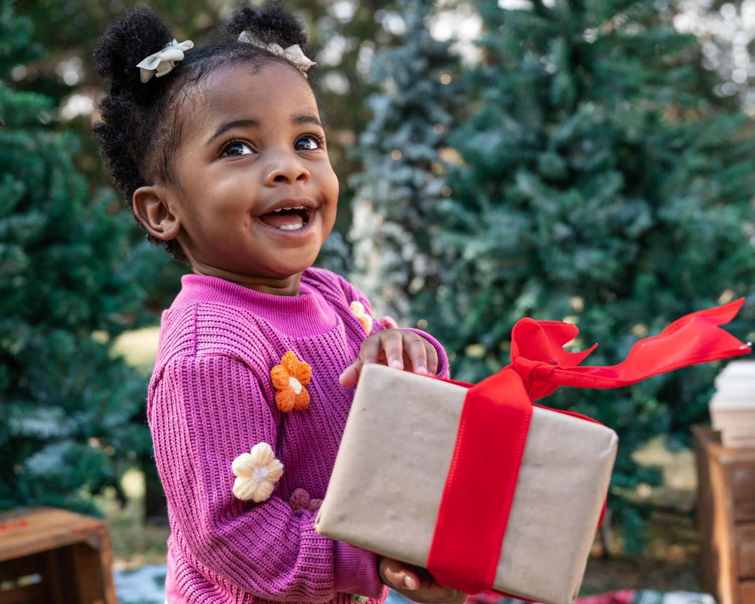 Excited child opening Christmas present wrapped in brown paper with red bow.