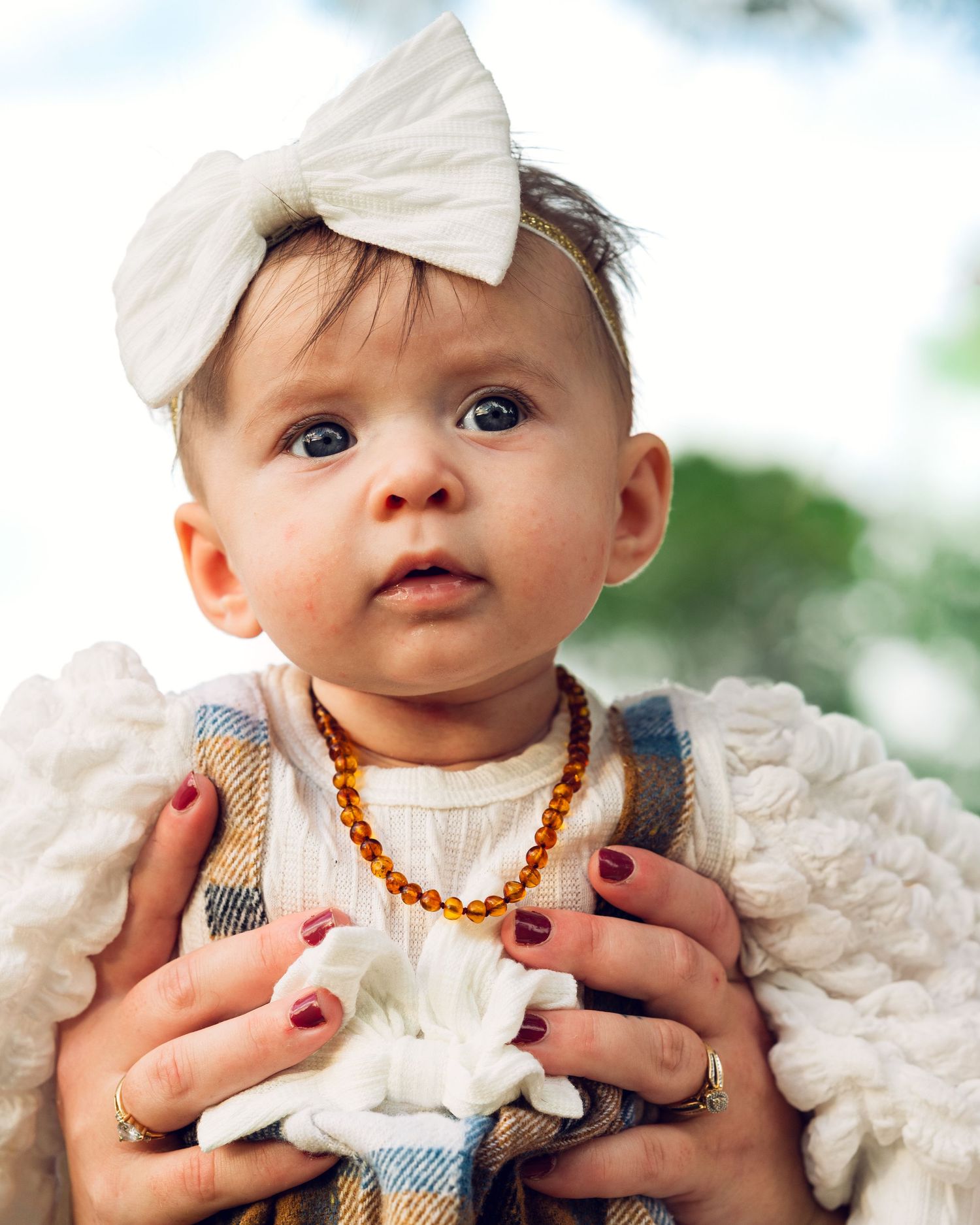 Close-up of a baby wearing a white bow headband and amber teething necklace.