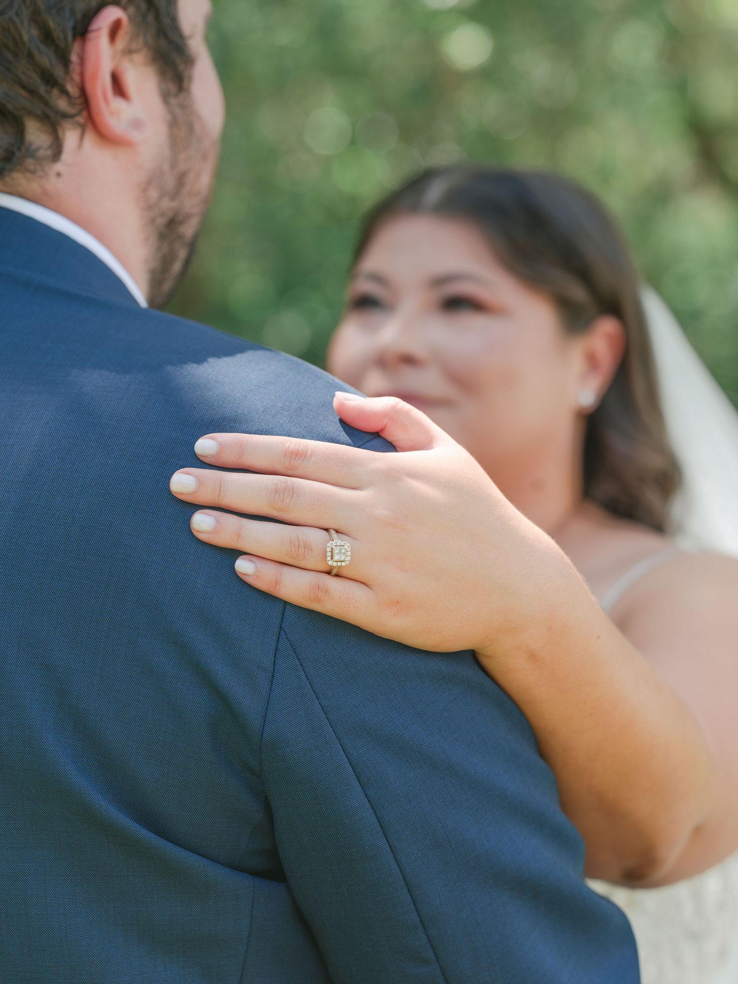 Bride rests her hand on groom's shoulder, showcasing a stunning halo engagement ring during their wedding ceremony.