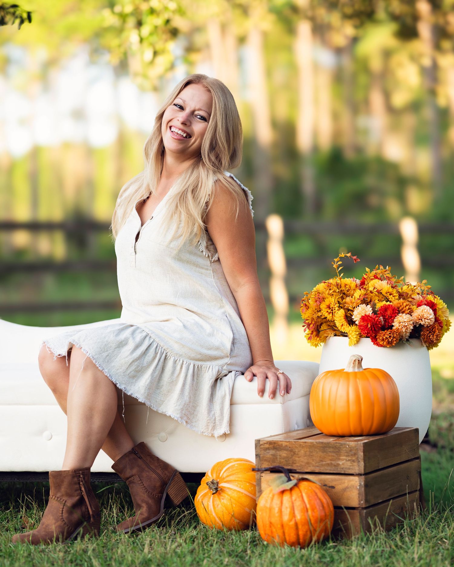 Fall themed outdoor photo shoot with white dress, wooden crates, orange pumpkins and autumn floral arrangements.