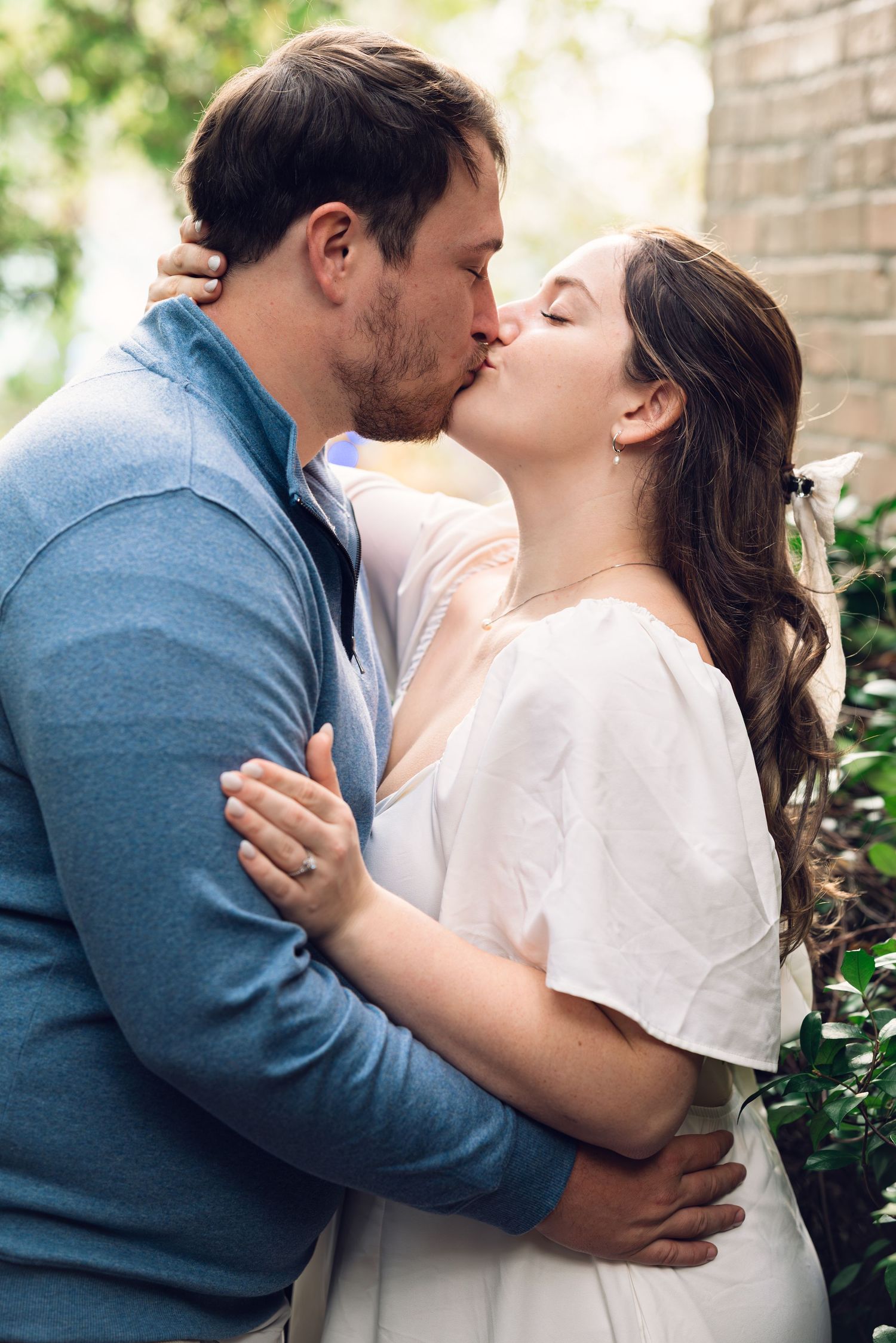An intimate romantic moment shared between a couple against greenery and brick.