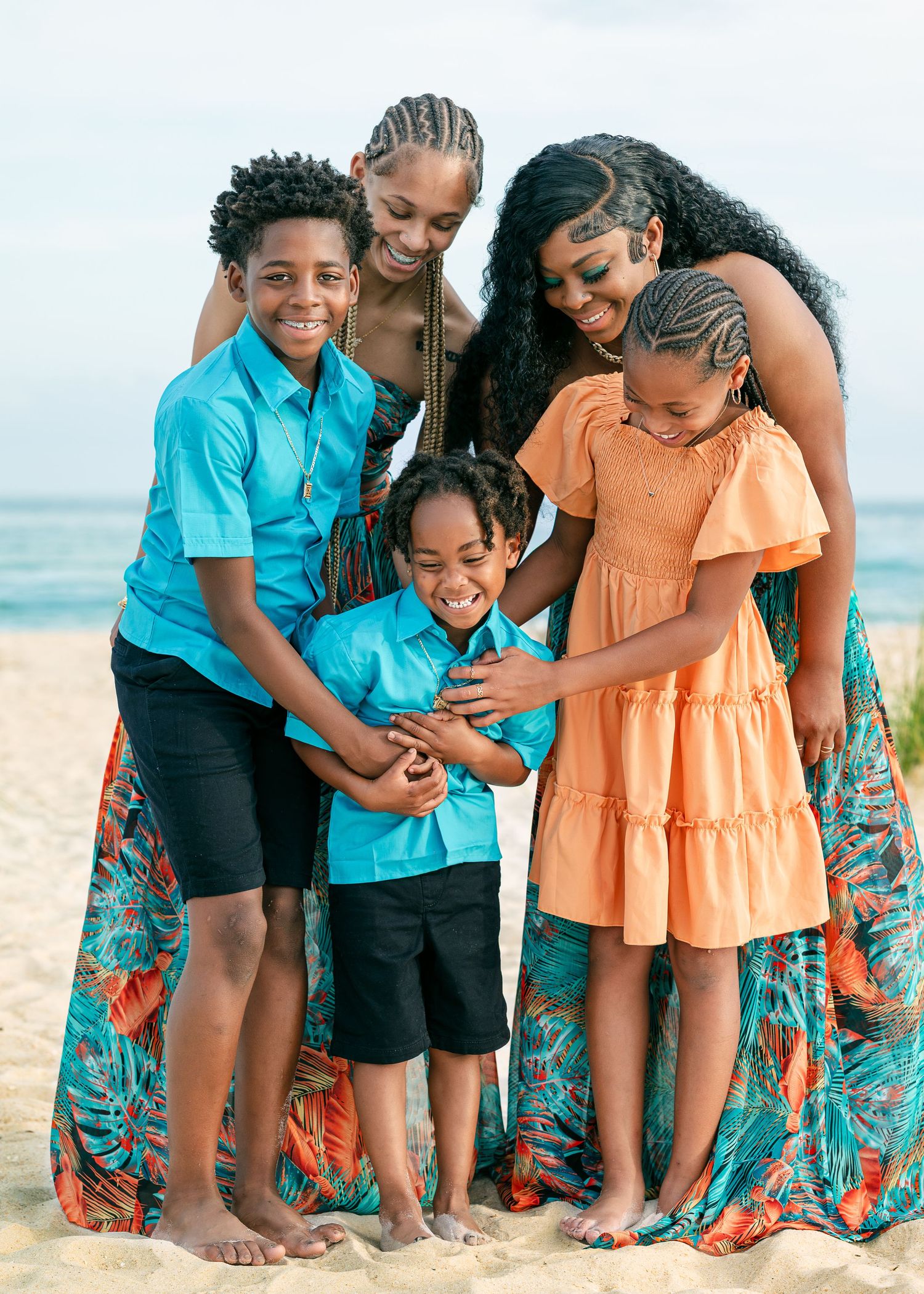 Family of five posing together on a sandy beach, wearing coordinating teal and orange outfits, smiling warmly.