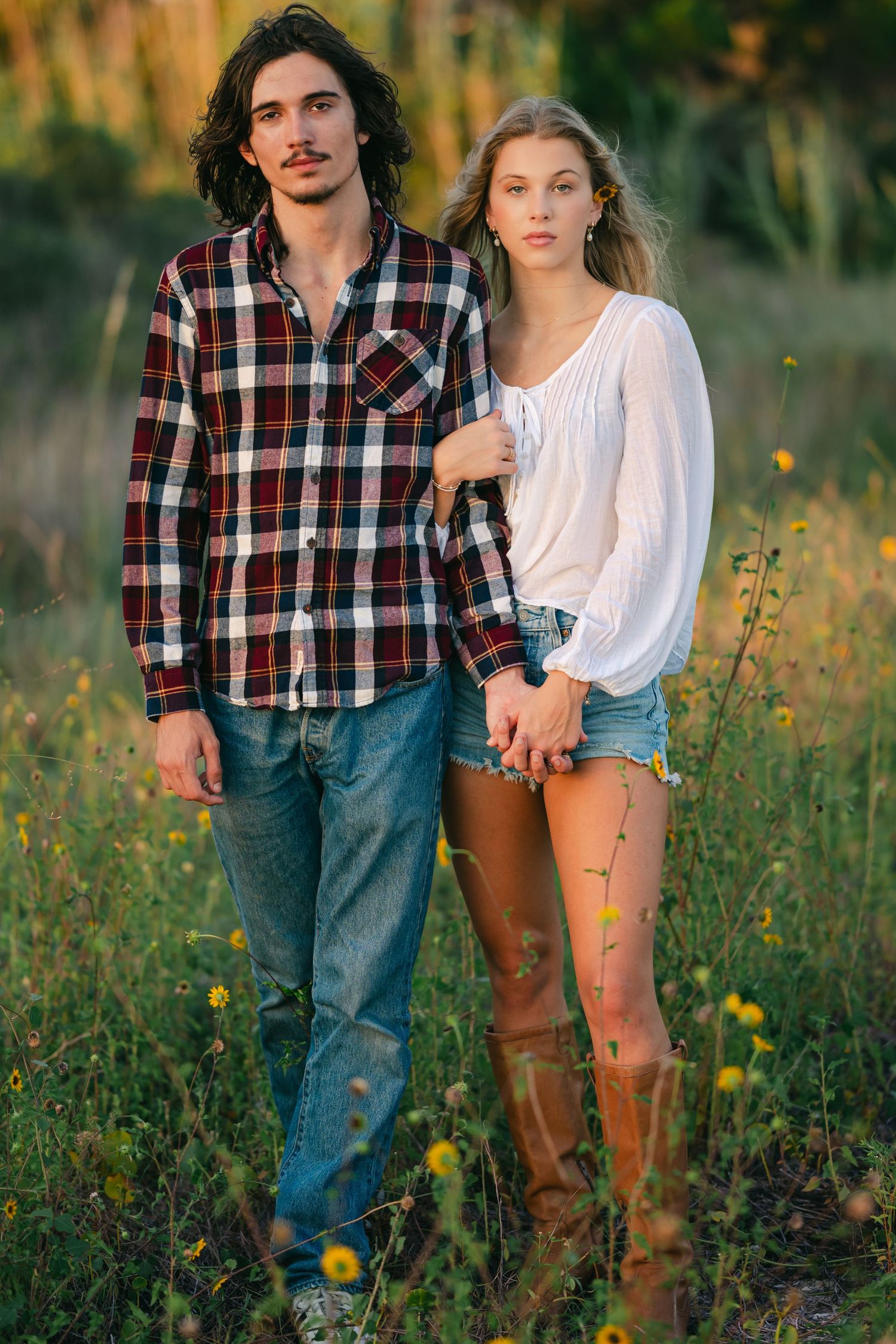 A couple in casual attire poses among wildflowers at golden hour.
