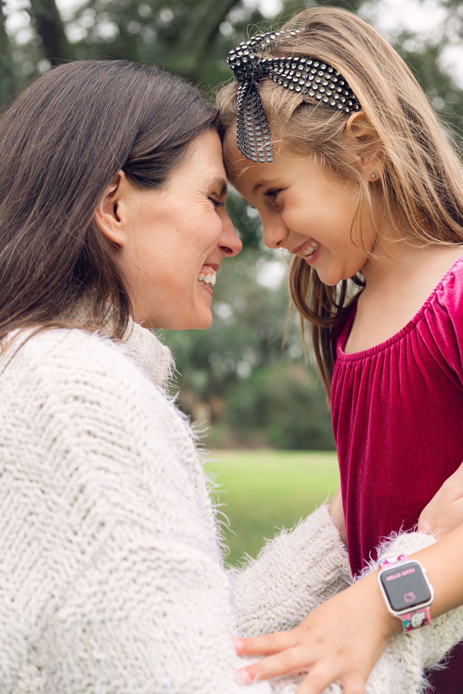 A tender moment between parent and child wearing a red velvet dress and cream sweater in an outdoor setting.