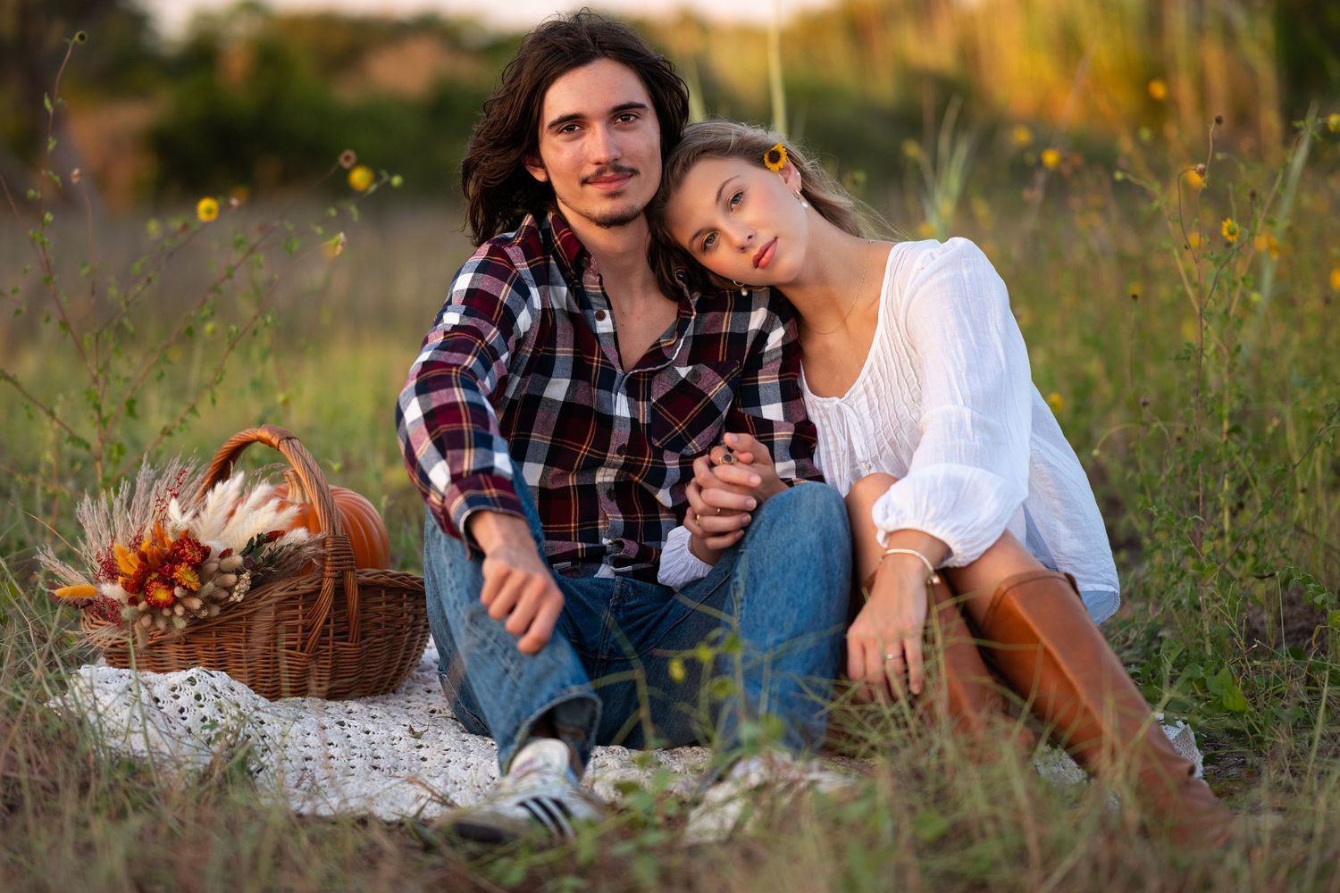 Couple enjoying a romantic afternoon picnic in a golden field with flowers and blanket.