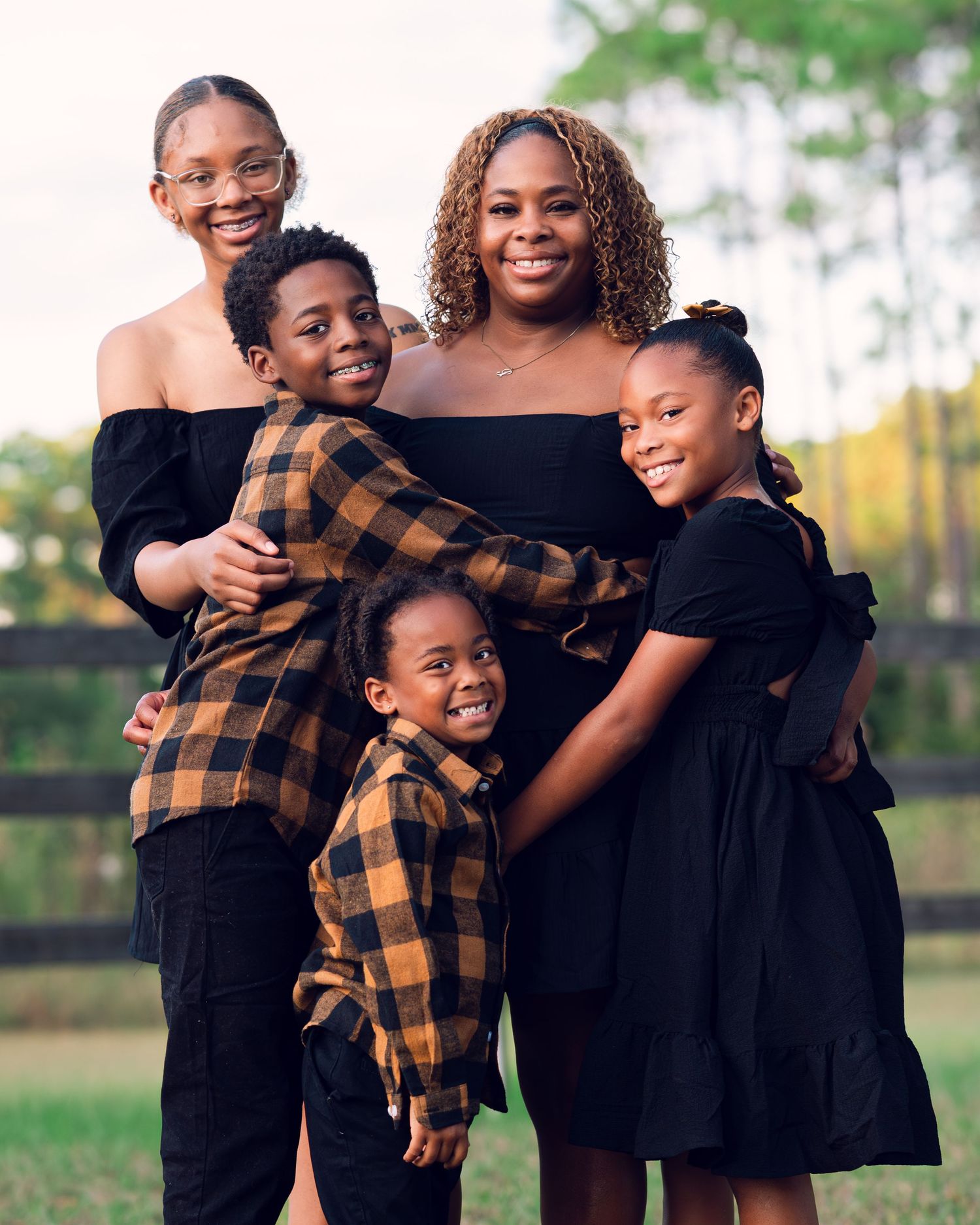 A family group poses together wearing coordinated black and brown outfits for fall photos.