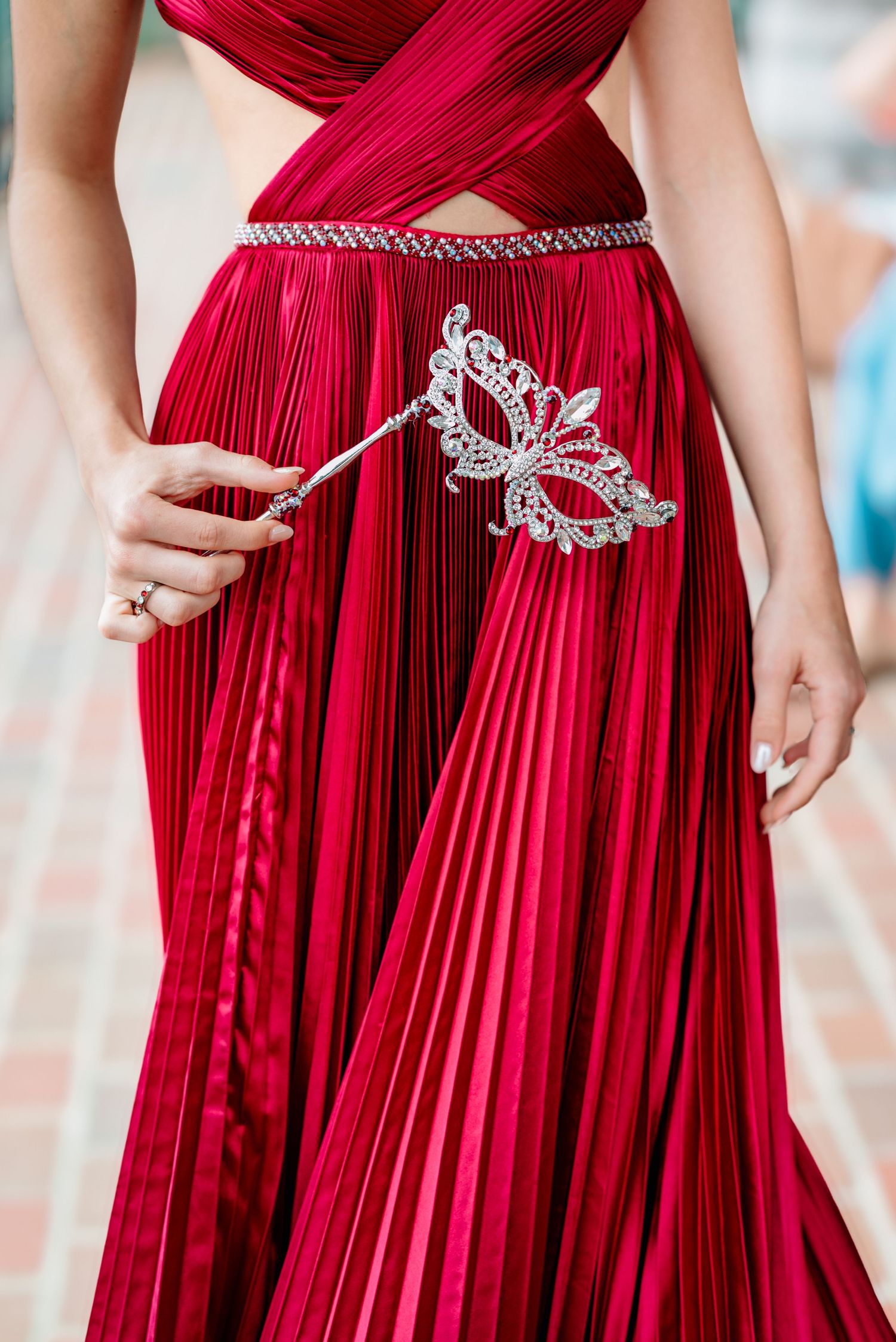 Details of a pleated red formal gown with crystal embellishments and intricate waist details.