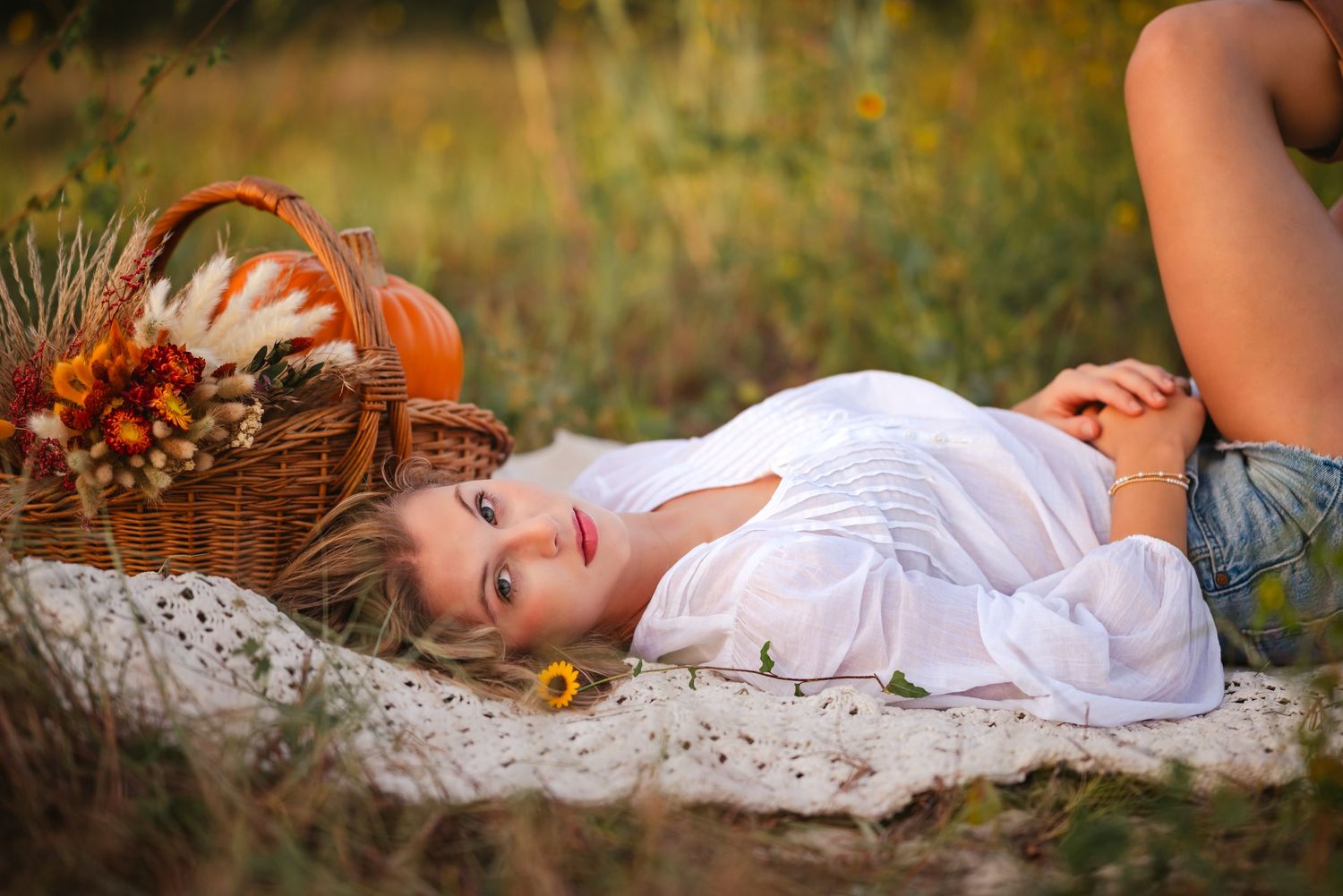 Dreamy outdoor picnic setup with white lace blanket and wicker basket in summer field.