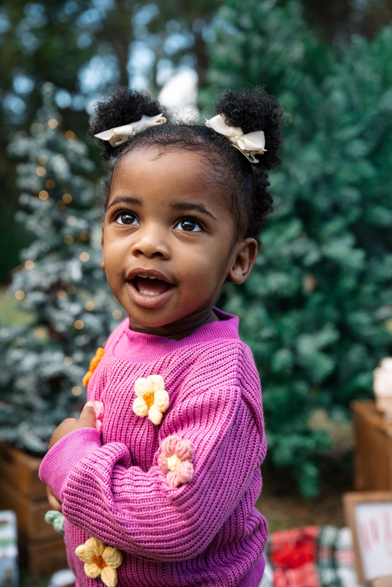 Child wearing pink sweater with flower details shows joy during holiday photoshoot.