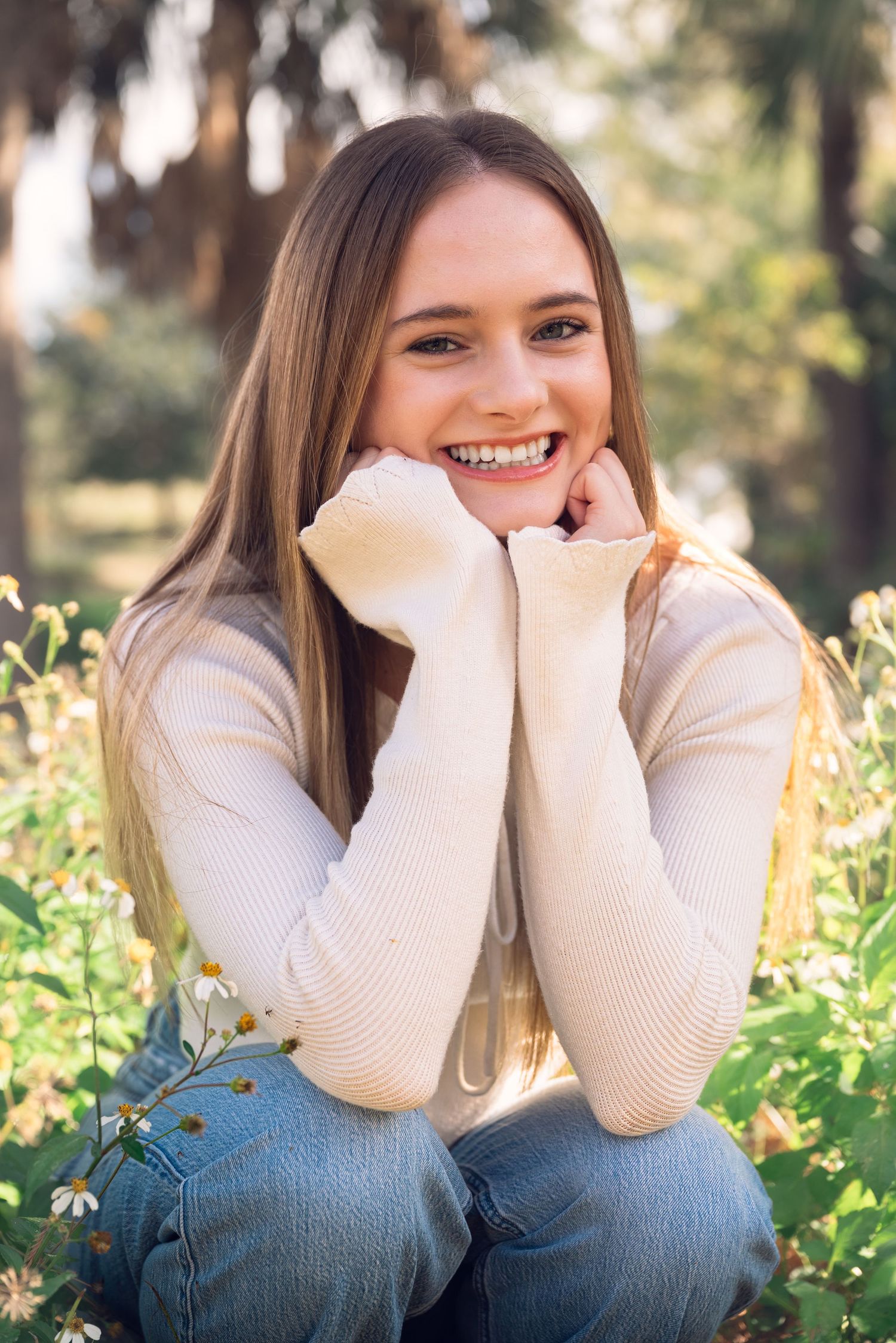 Playful outdoor portrait in cream sweater and jeans amid blooming wildflowers.