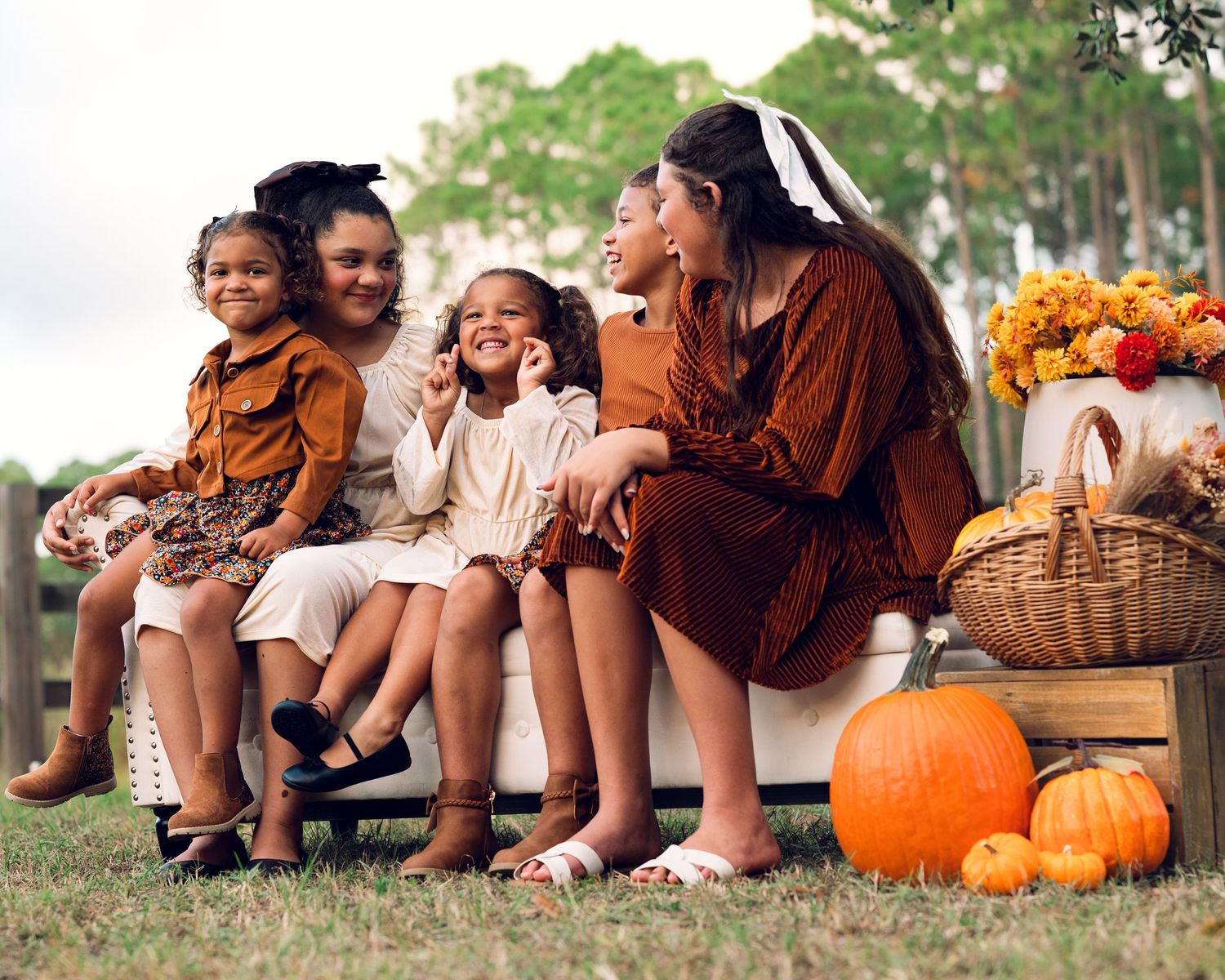 A fall family photo with pumpkins and flowers features coordinated brown and white outfits.