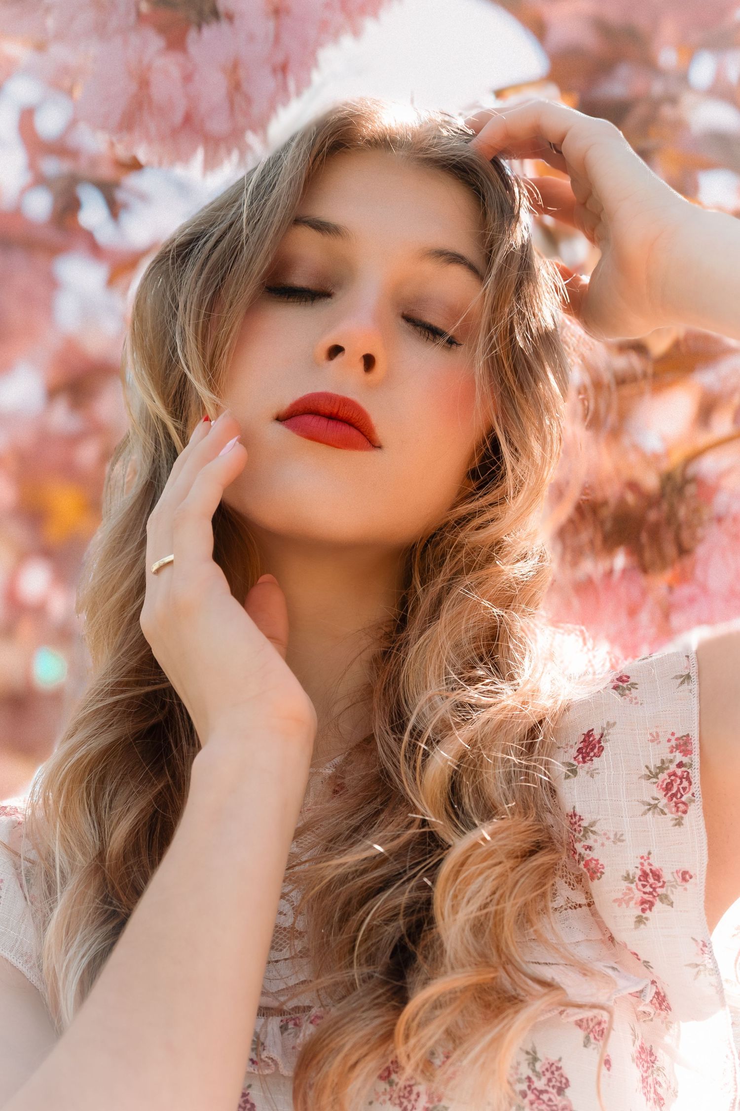 Dreamy portrait of woman with red lips against pink cherry blossoms.