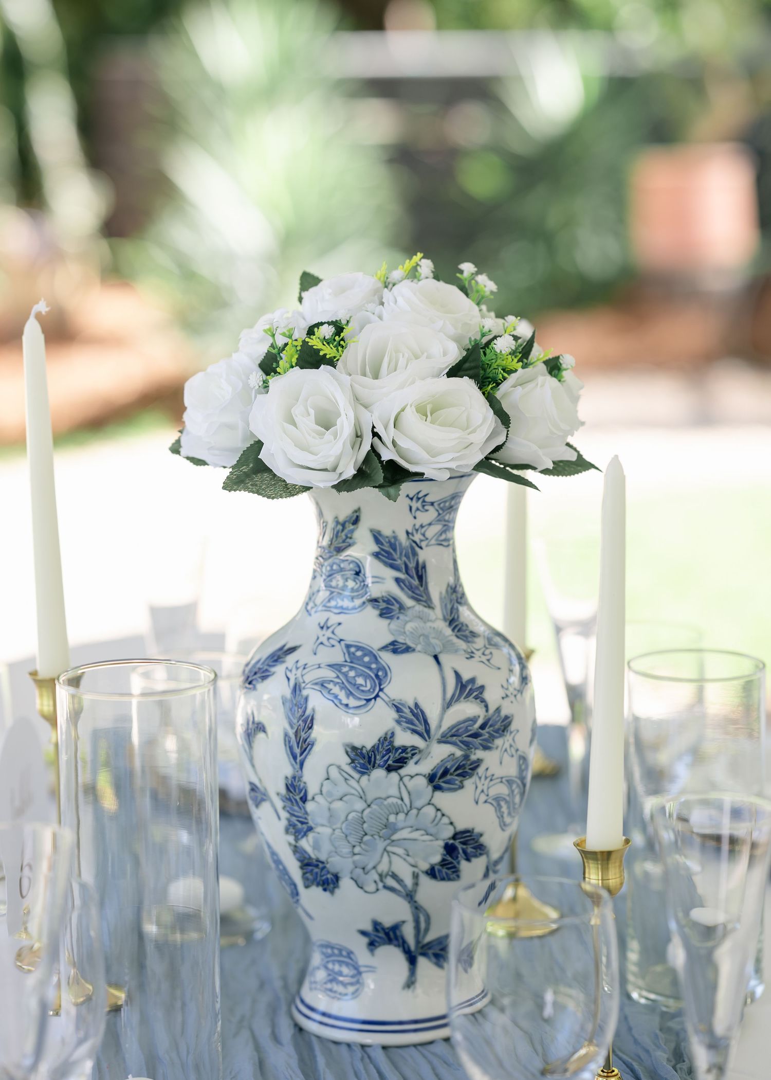 Blue and white floral porcelain vase centerpiece with white roses, flanked by taper candles on an elegant tablescape.