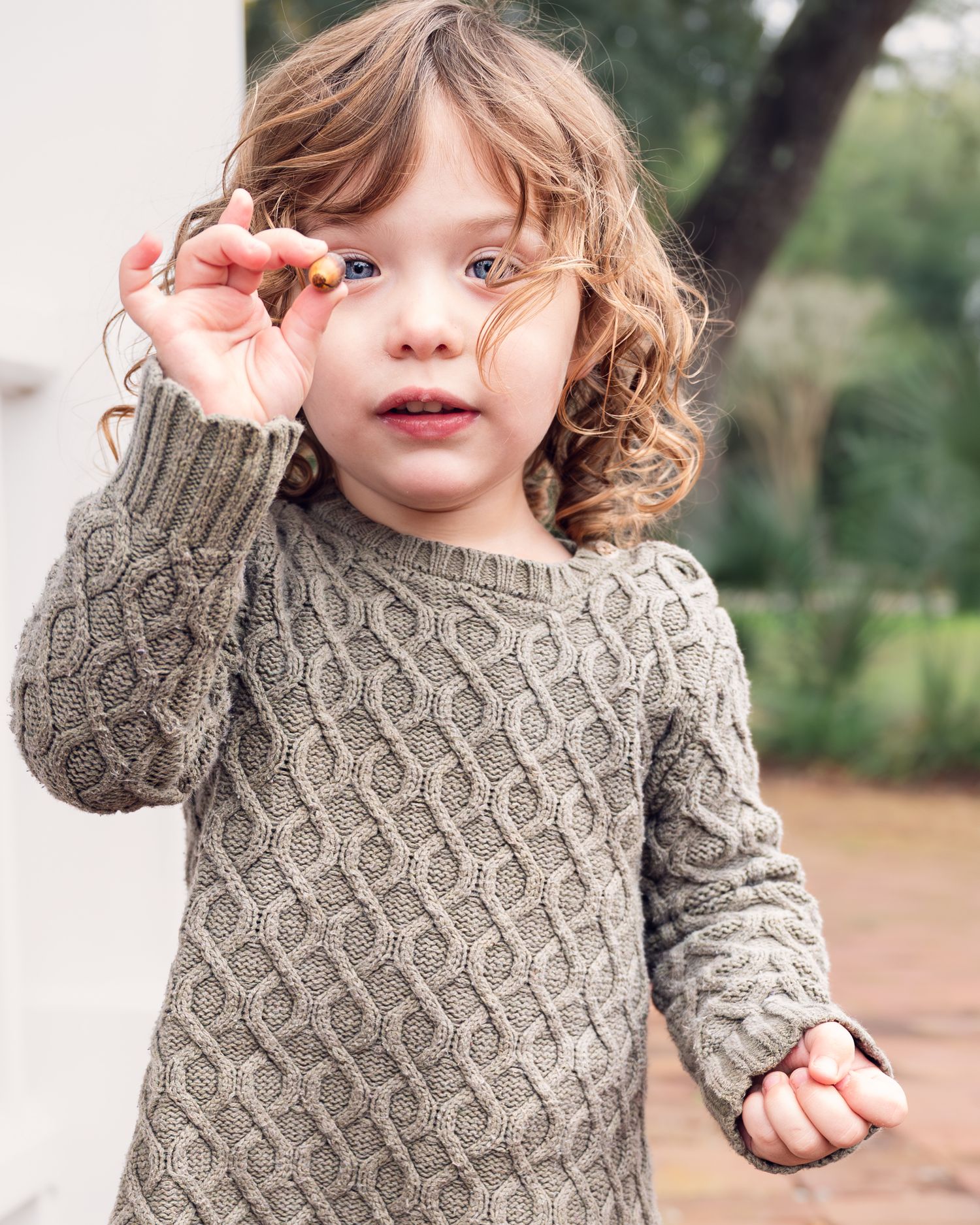 Close-up portrait of young person wearing gray cable knit sweater outdoors.