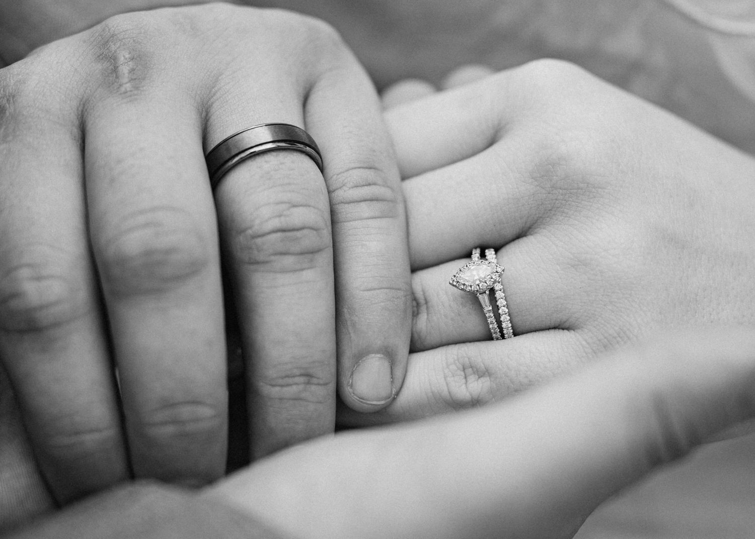 Black and white photo of a couple holding hands, showcasing a mens tungsten wedding band and womens diamond engagement ring set.