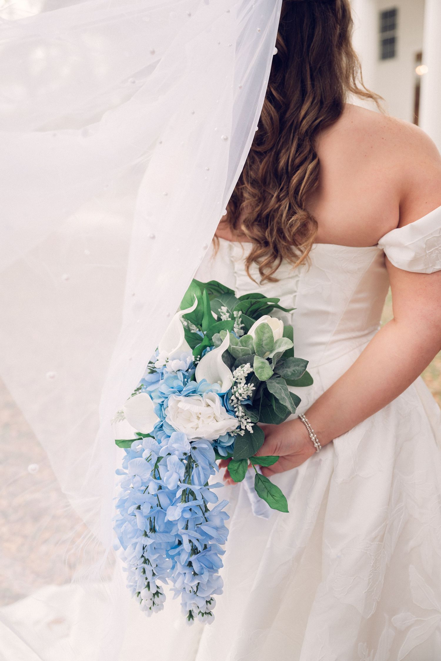 A bridal bouquet featuring light blue delphinium flowers and green eucalyptus leaves against a white dress.