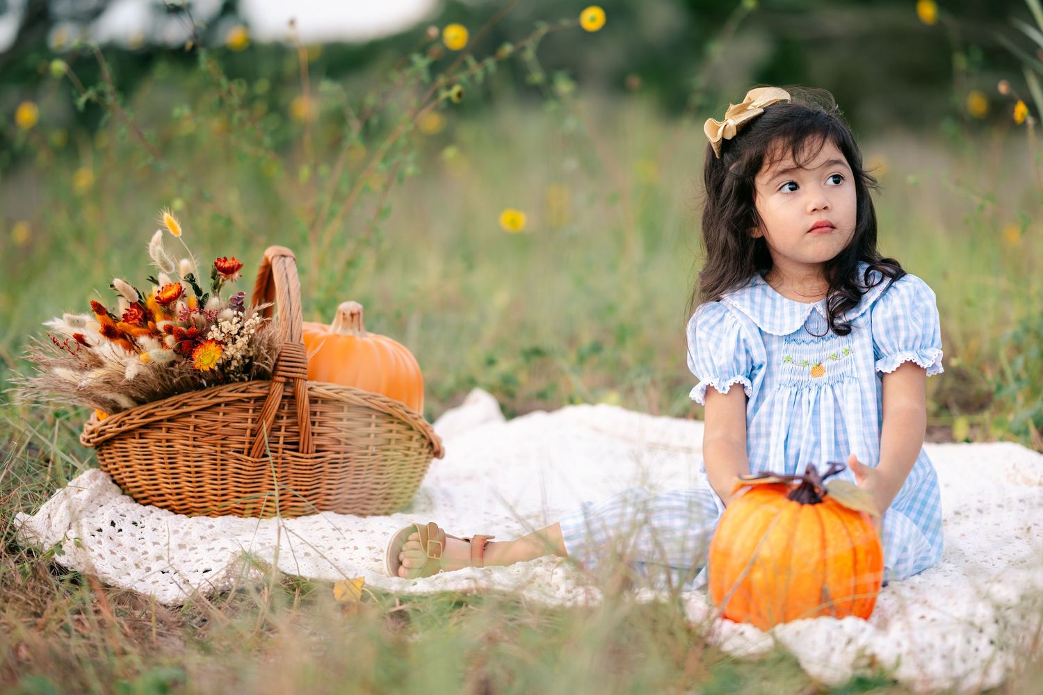 A harvest-themed outdoor scene with pumpkins and wicker baskets on a white blanket.