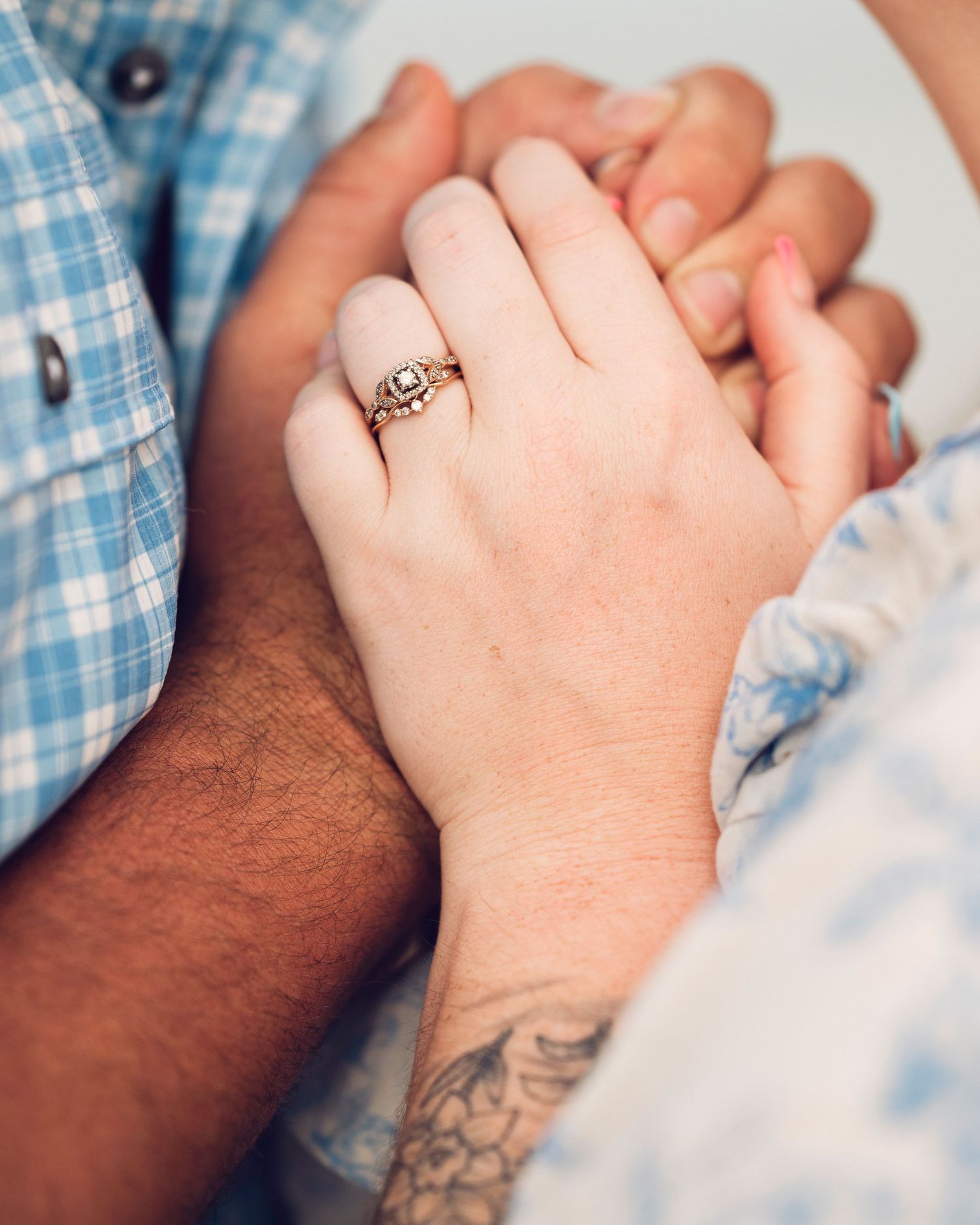 Close-up of intertwined hands showing an engagement ring and tattoo details.