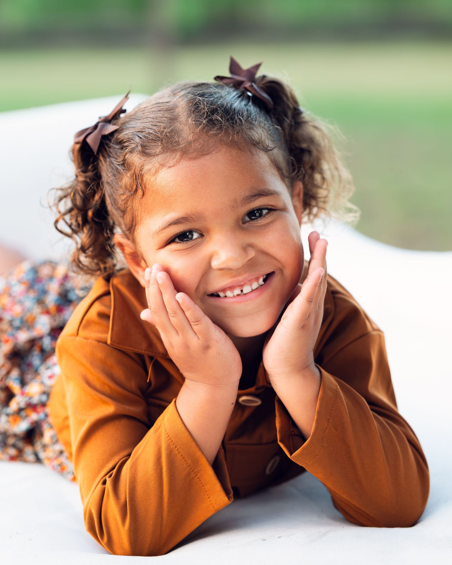 A joyful portrait of someone in a brown jacket resting their face in their hands.