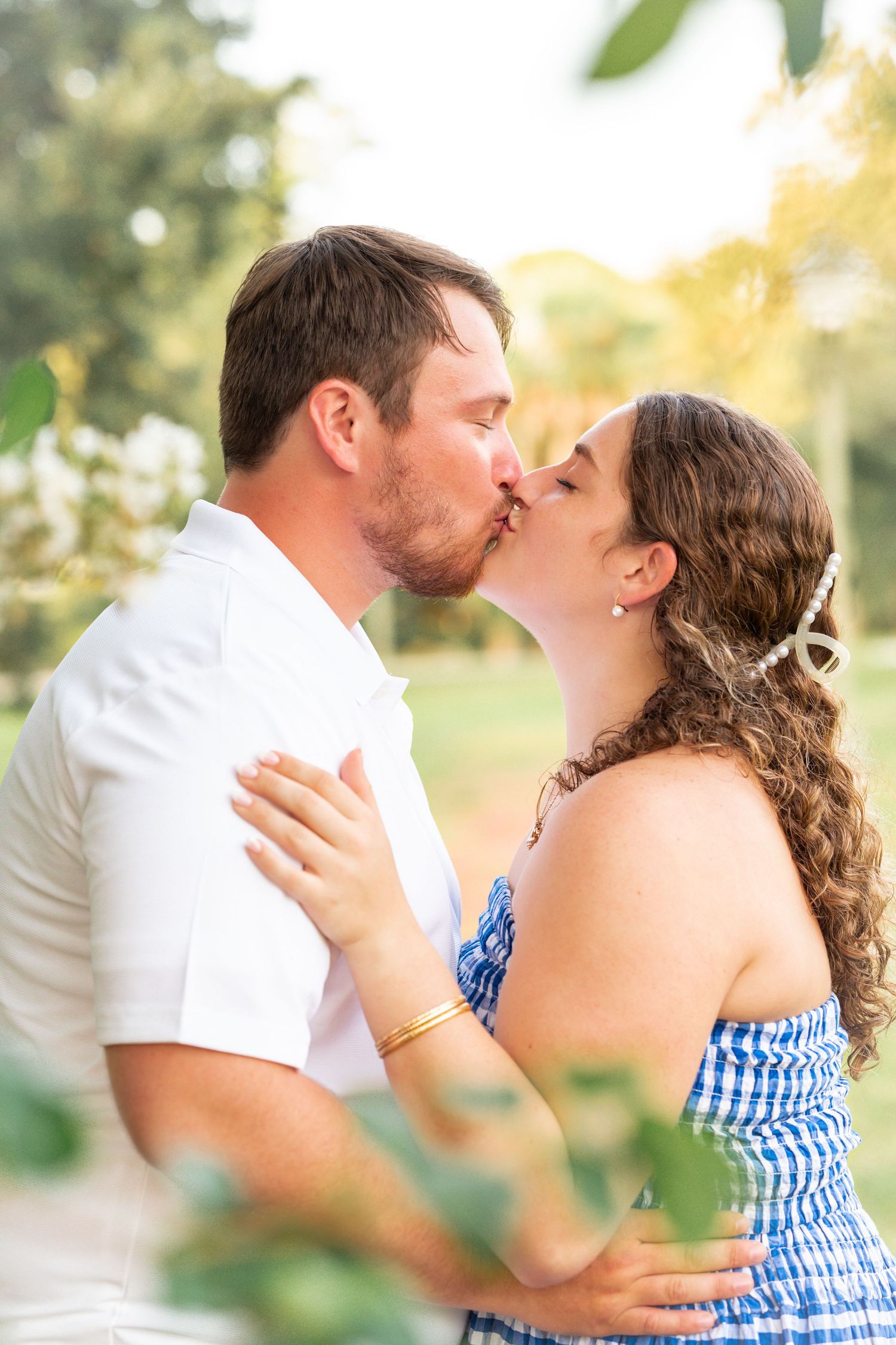 Romantic outdoor engagement photo with blue gingham dress and greenery.