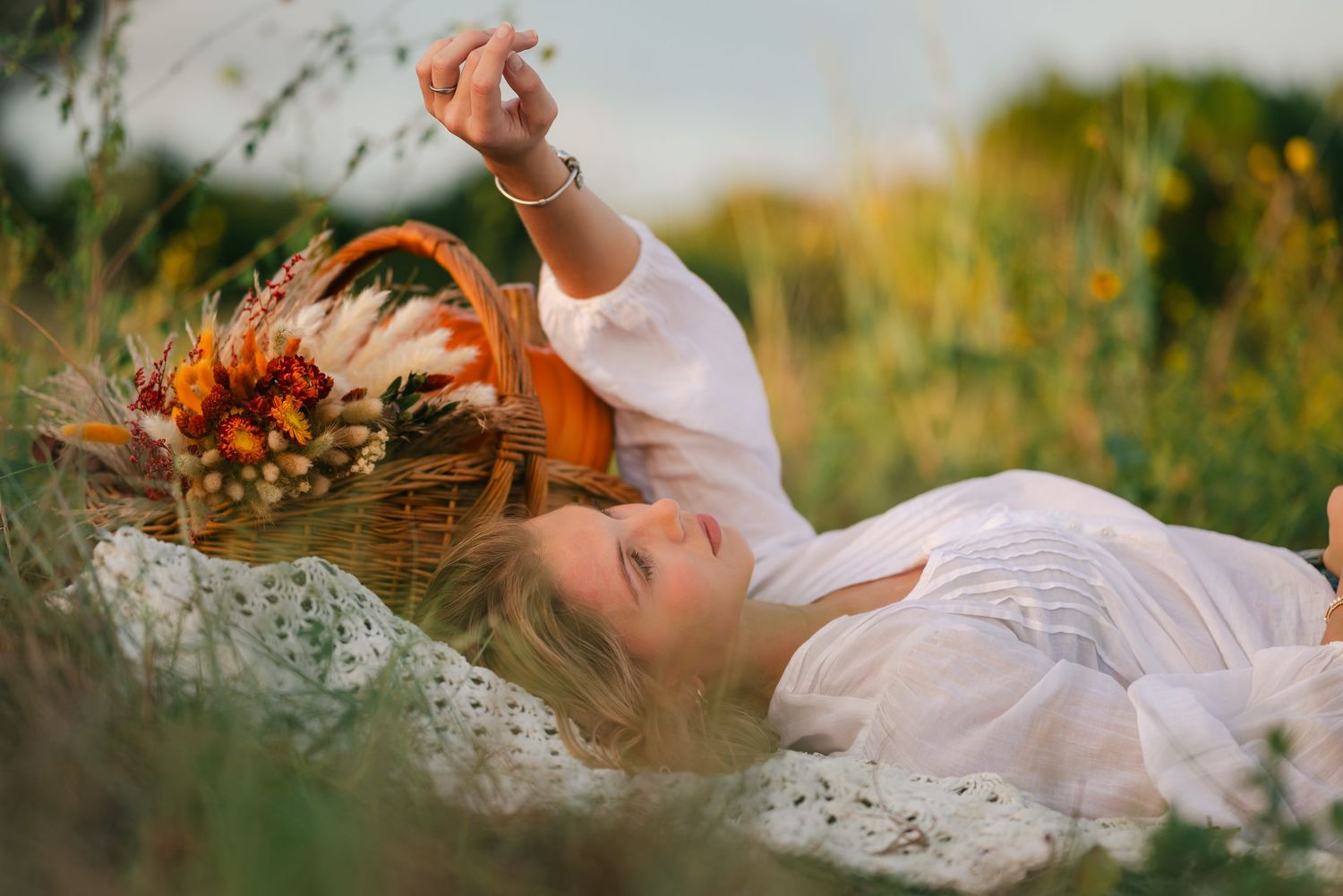Romantic picnic scene in a sunlit meadow with white blanket and wicker basket among wildflowers.