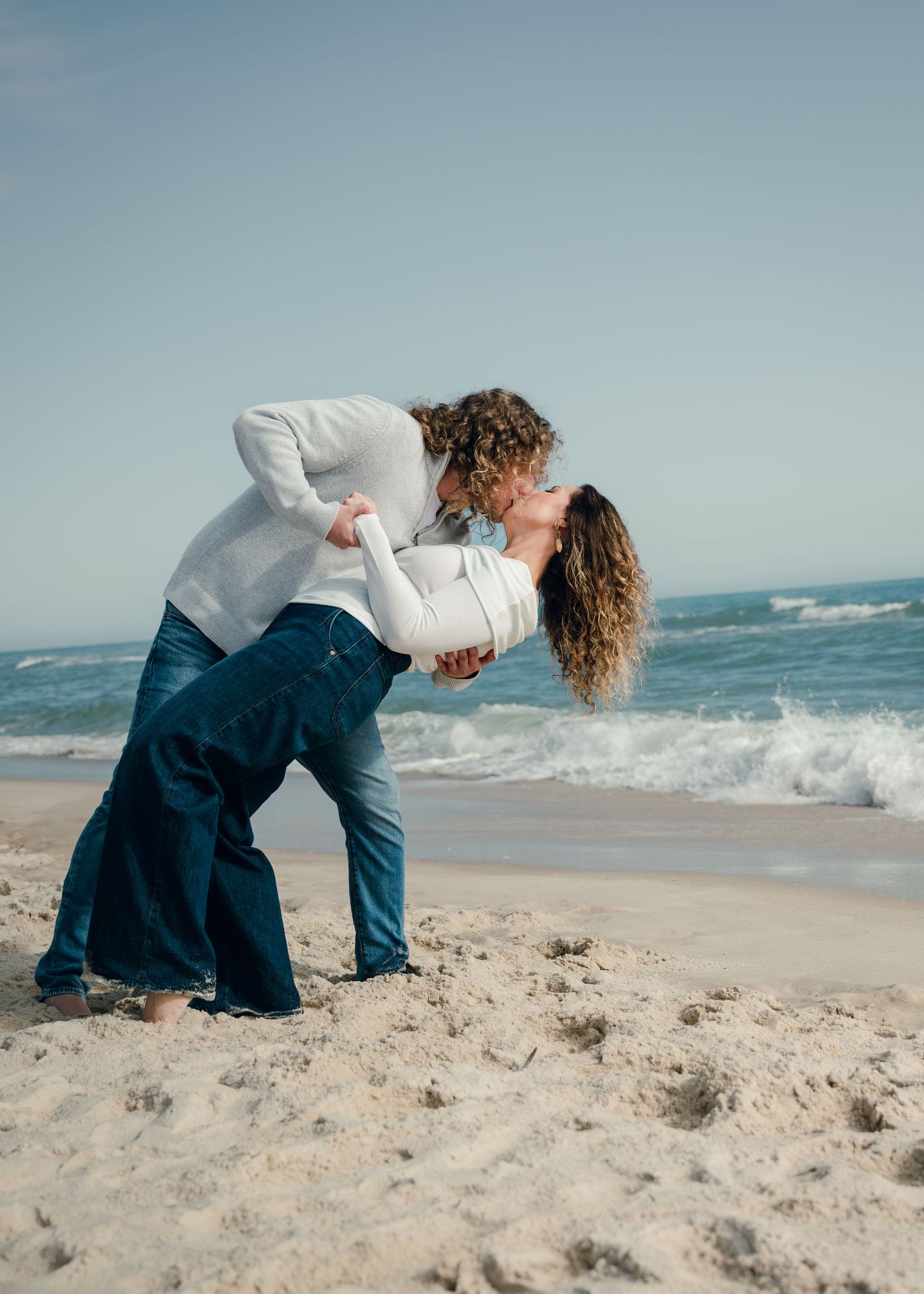 A couple shares a romantic moment on a sandy beach with crashing waves in the background.