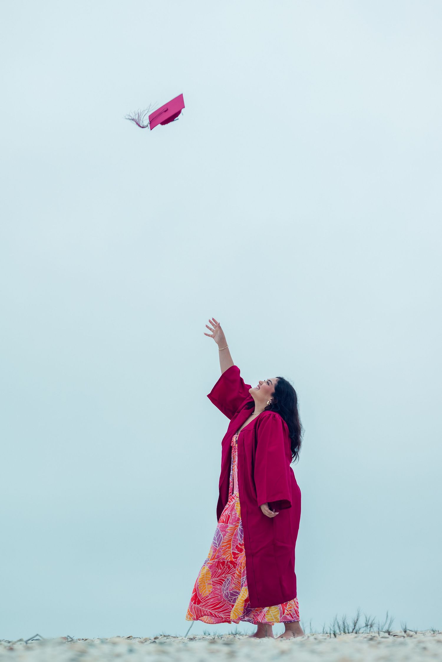 A person in a red dress releases a pink butterfly into the pale blue sky on a grassy hilltop.