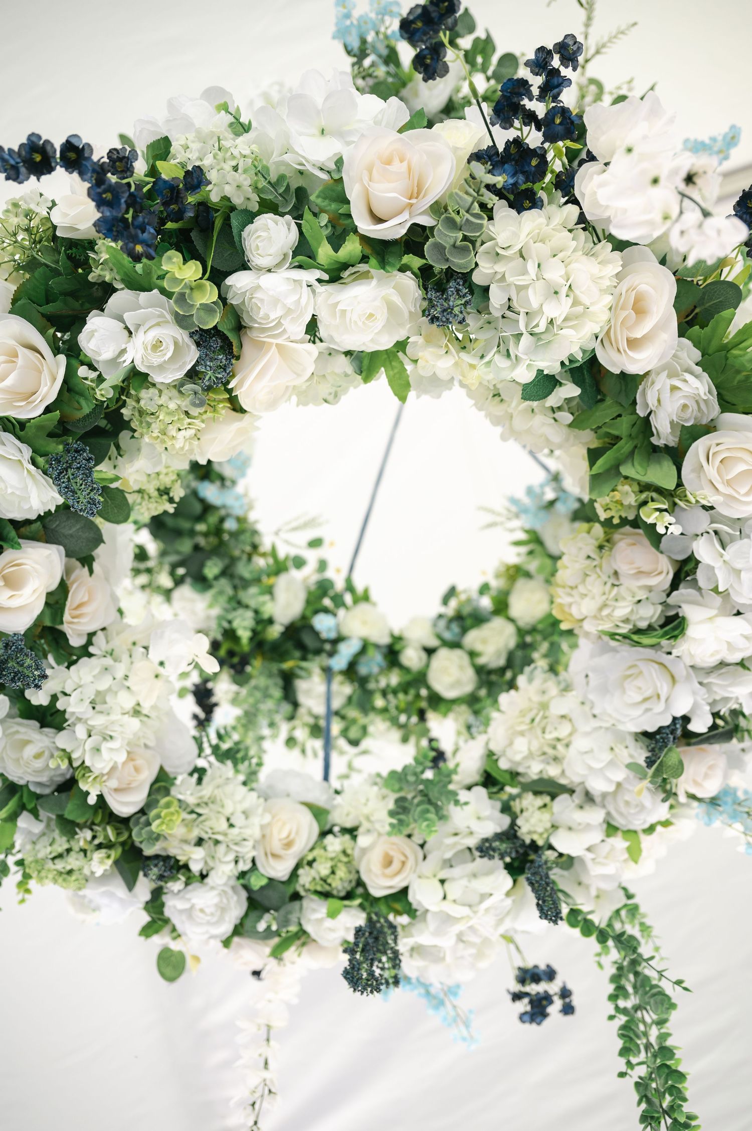 Elegant floral wreath with white roses, hydrangeas, and green foliage accented with dark blue berries for a wedding.
