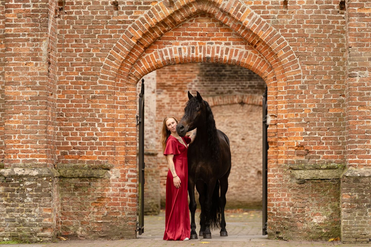 Spaanse merrie samen met eigenaresse in sjieke rode jurk bij de ingang van de oude kerk in Dongen
