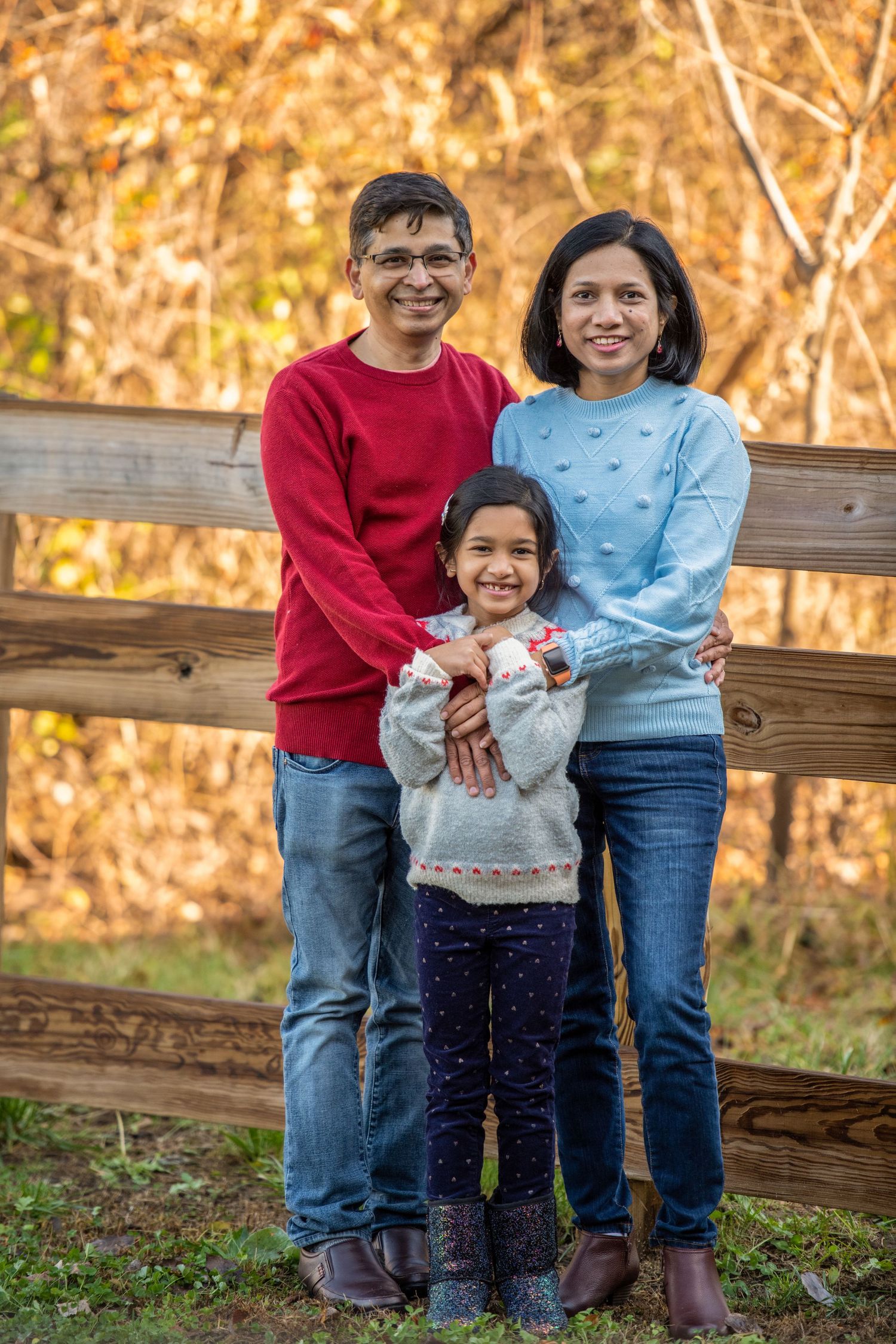 Family portrait of three members sitting on wooden fence during golden autumn afternoon.