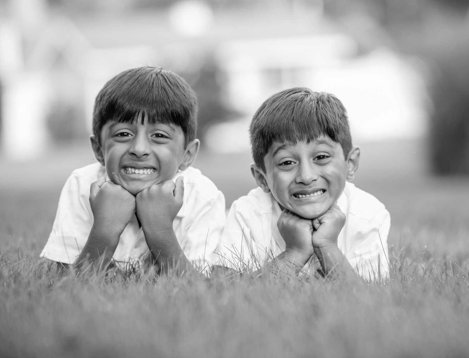 Black and white portrait series of children lying in grass with joyful expressions.
