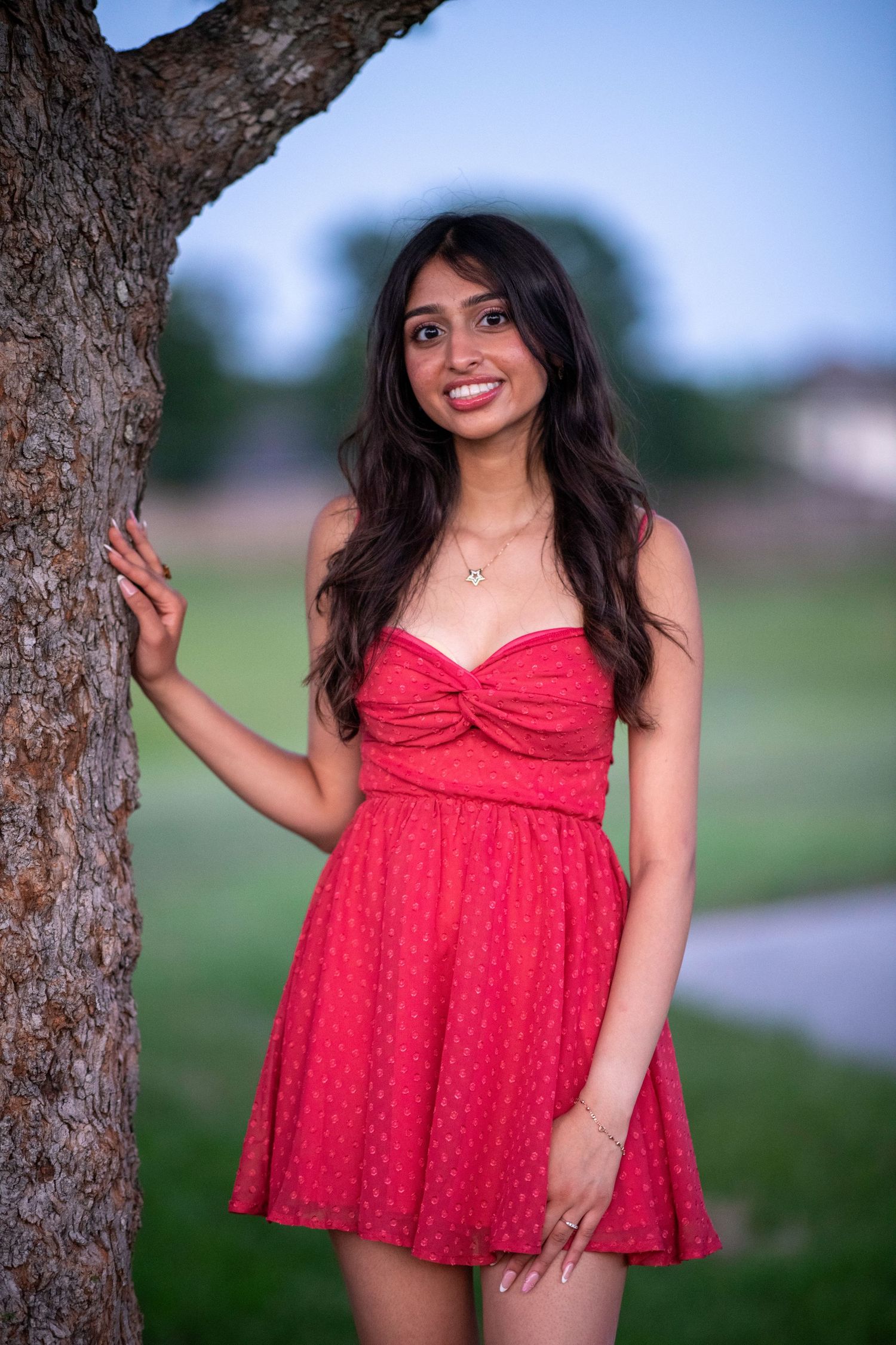 A red polka dot sundress is featured in an outdoor portrait session near a tree.
