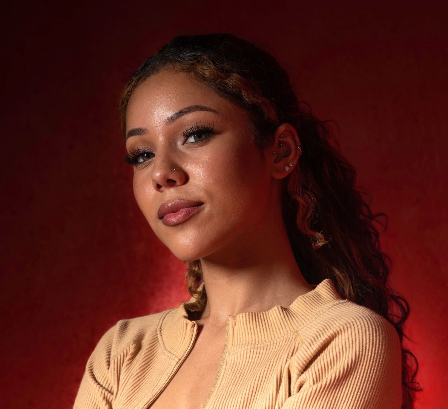 A person in a peach-colored sweater poses against a dark red background with dramatic lighting.