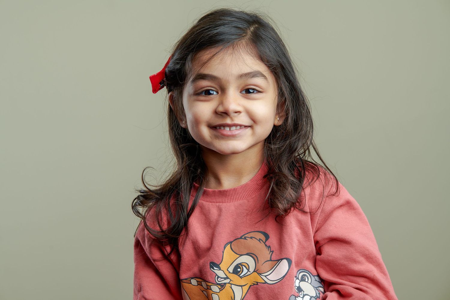 Child wearing a pink sweatshirt with cartoon character design standing against light background.