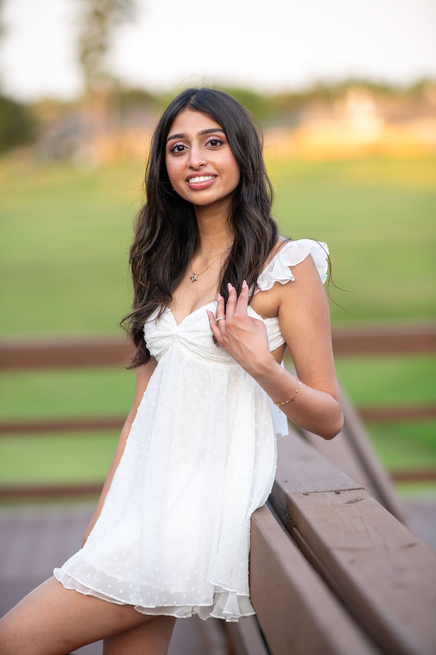 A white flowy dress is showcased in an outdoor photoshoot with warm sunset lighting.