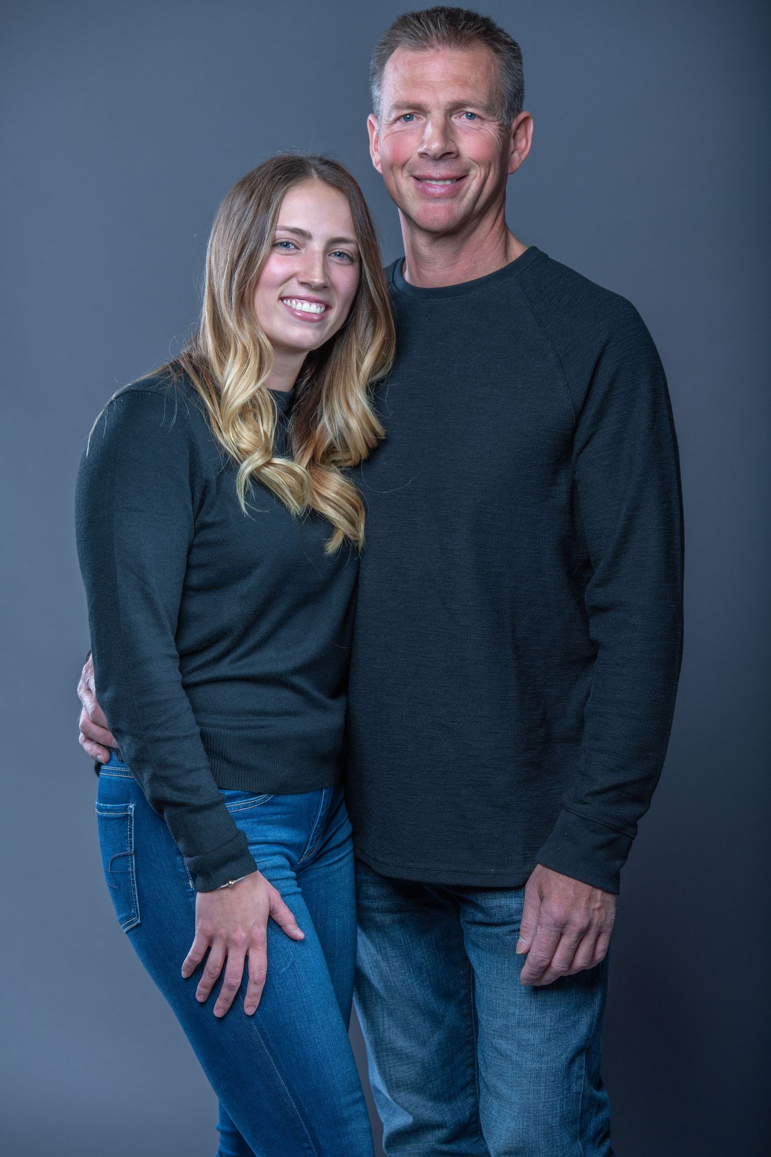Studio portraits of couple in matching black sweaters against dark grey background.