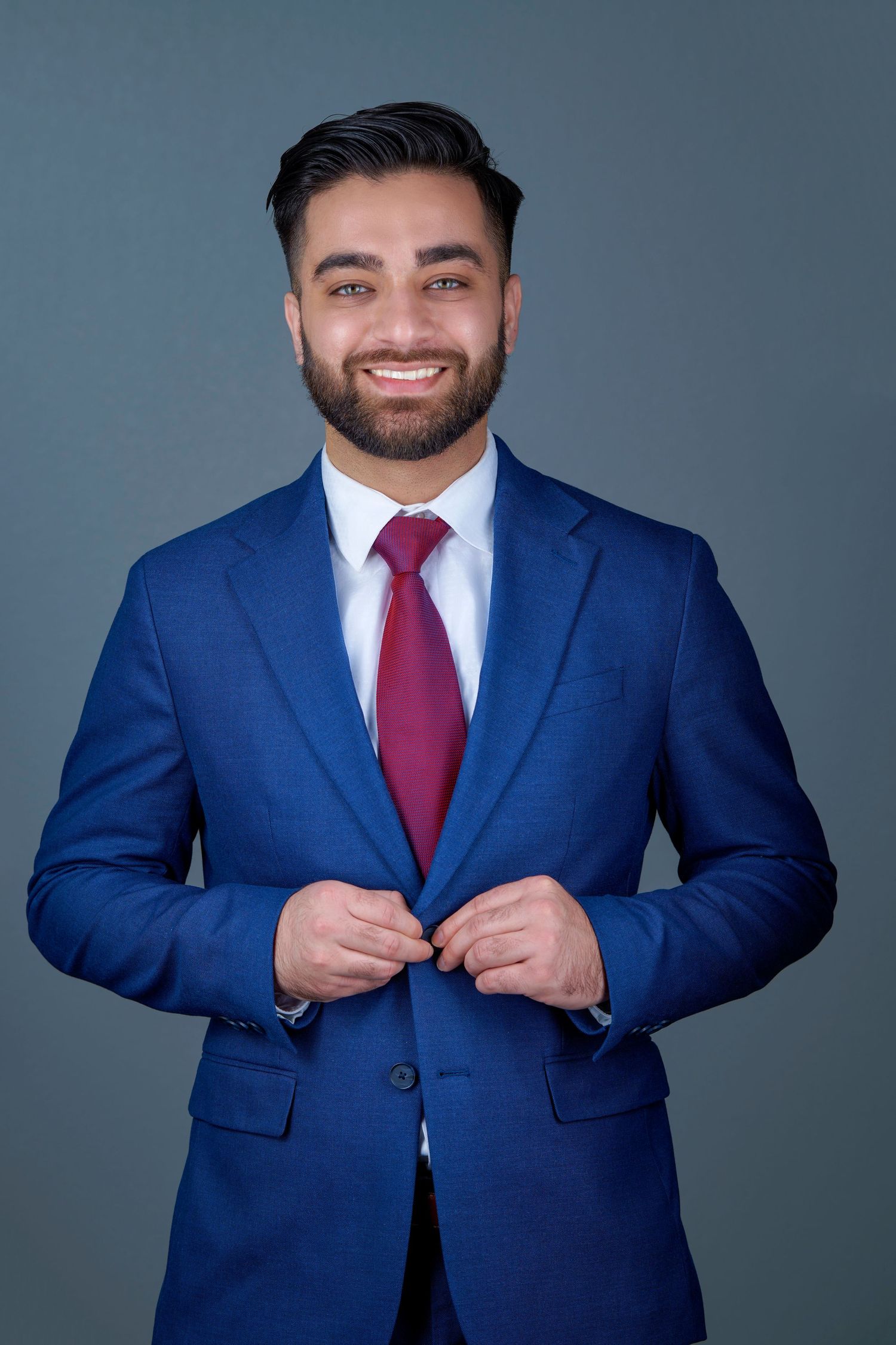 Professional wearing a navy blue suit and burgundy tie buttons jacket in studio portrait sequence.