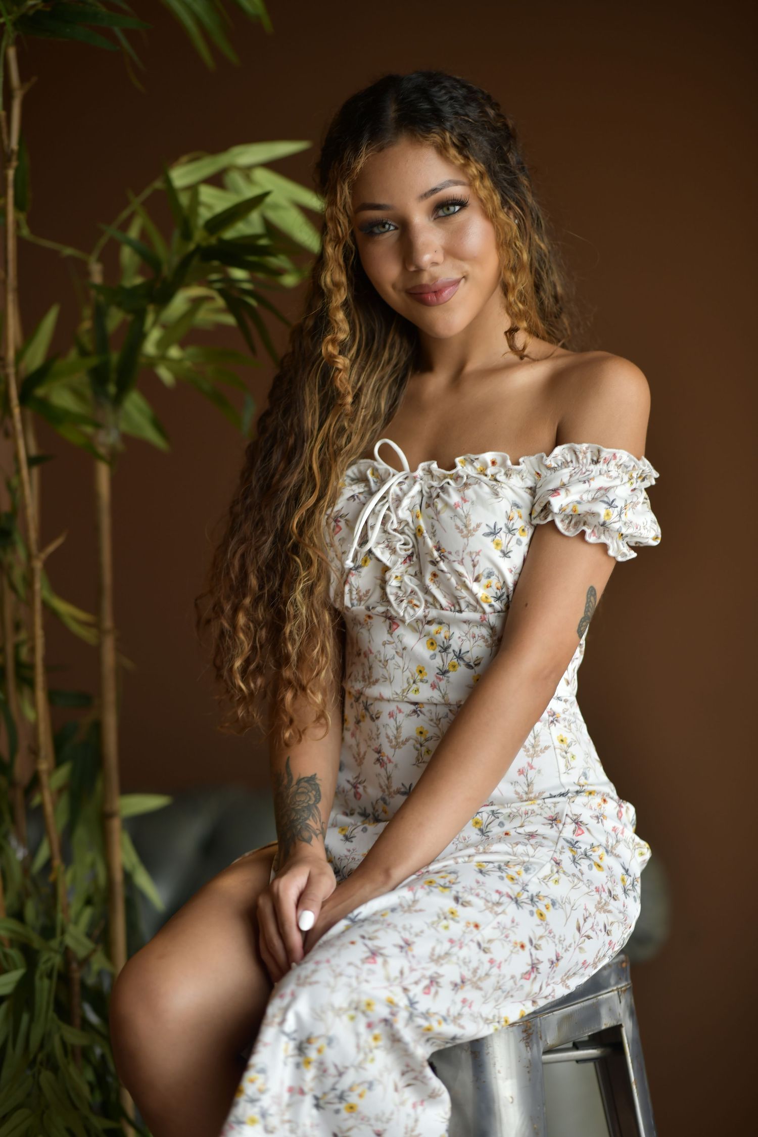 A floral off-shoulder dress is highlighted in a moody indoor portrait session with plants.