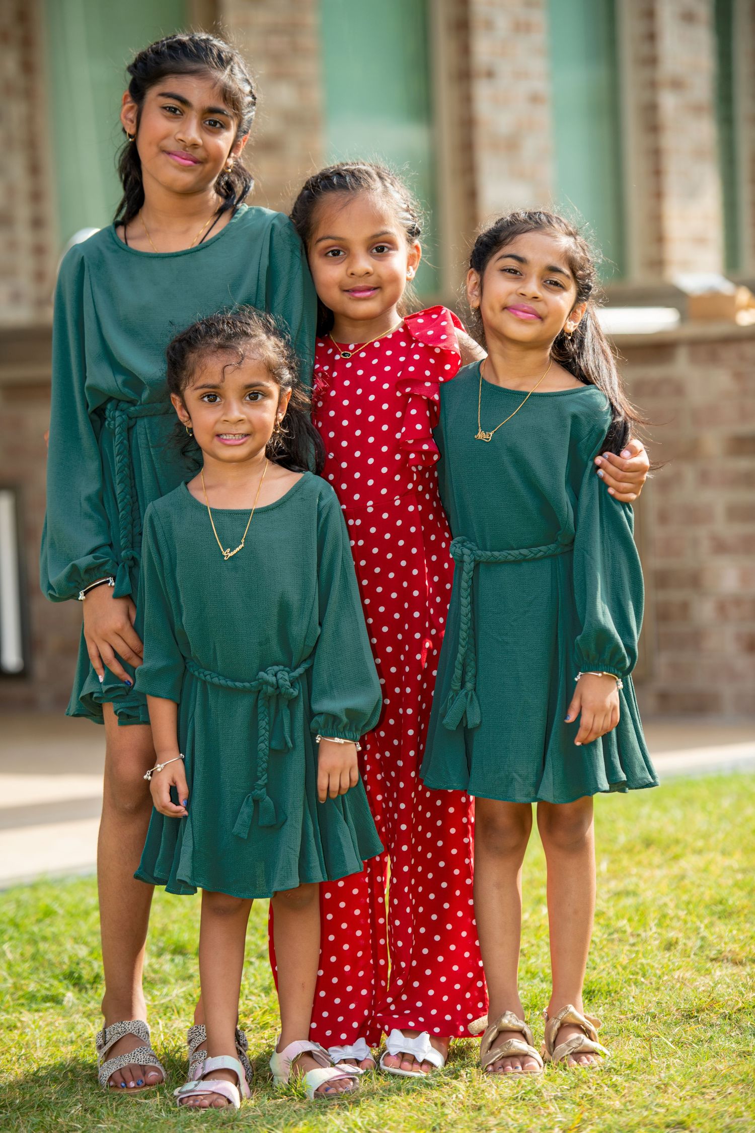 Group photo of siblings in coordinated green dresses and red polka dot dress on grass.