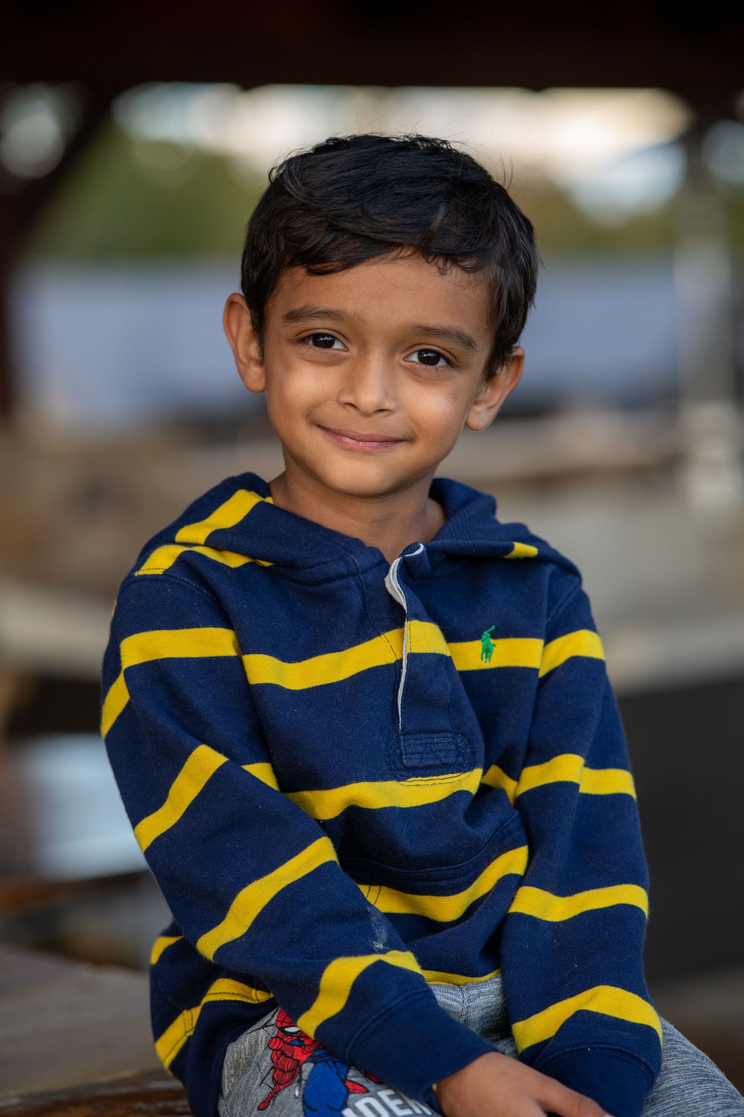 Child wearing navy and yellow striped hoodie smiling in outdoor portrait.