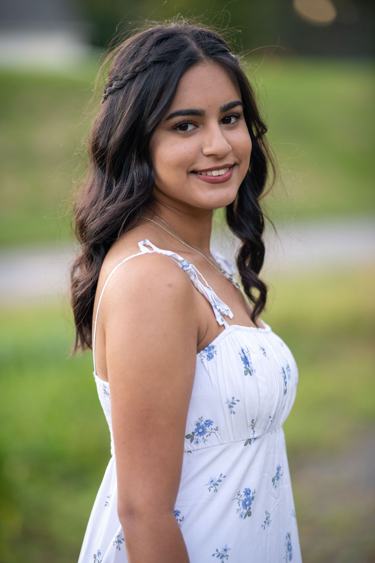 A white summer dress with blue floral prints is captured in an outdoor garden setting.