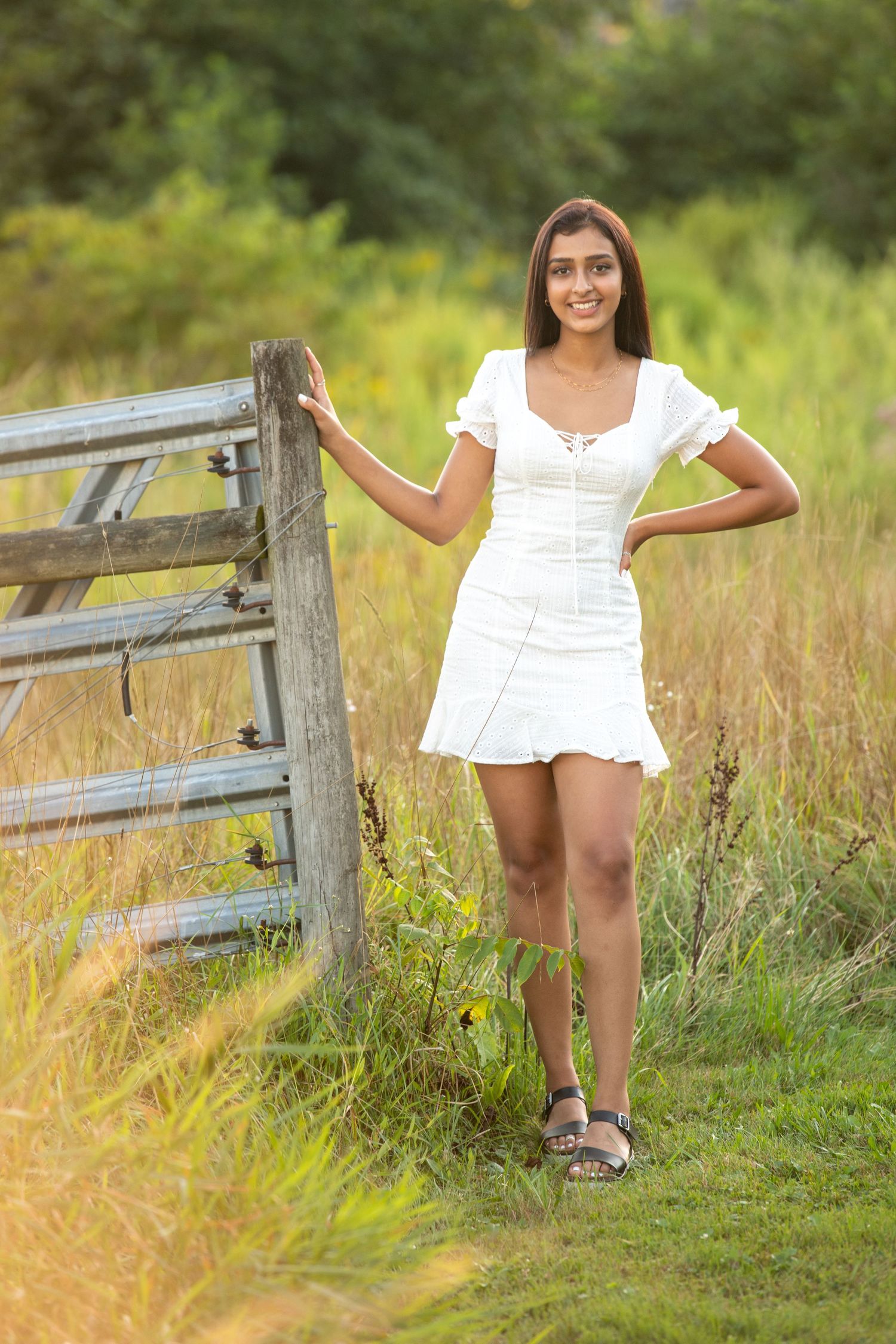 A summery white outfit is captured near a rustic wooden fence in tall grass.