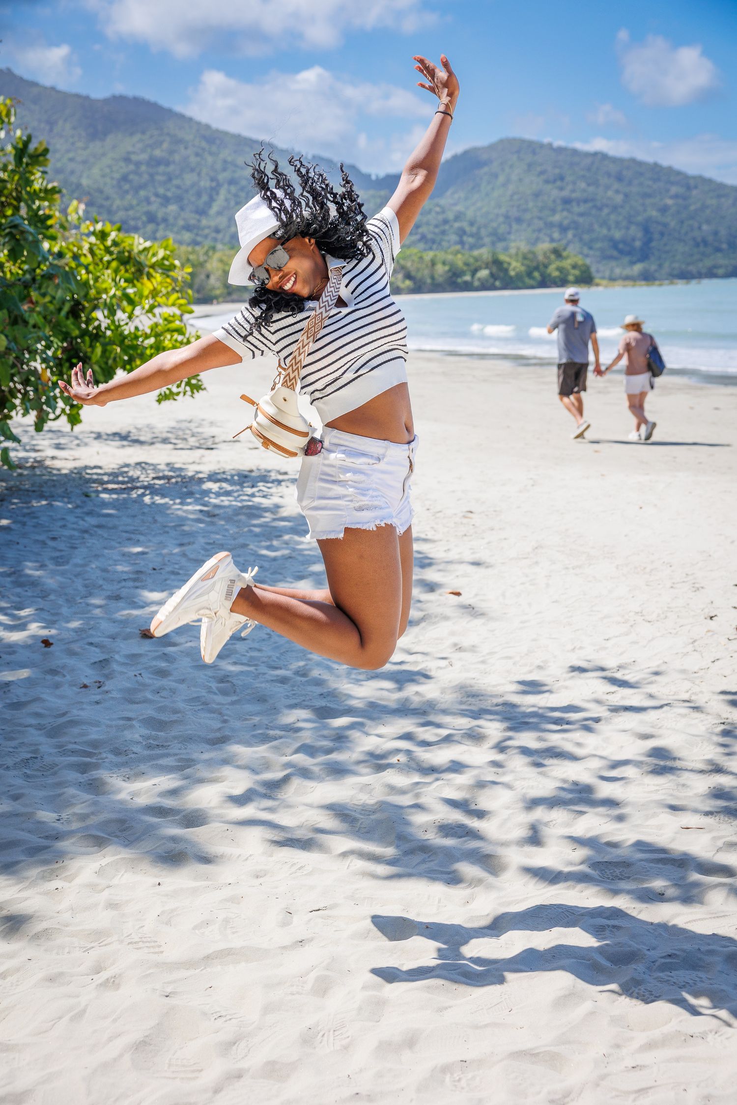 A sequence of jumping shots on a pristine beach with mountains in the background shows playful beach activities.