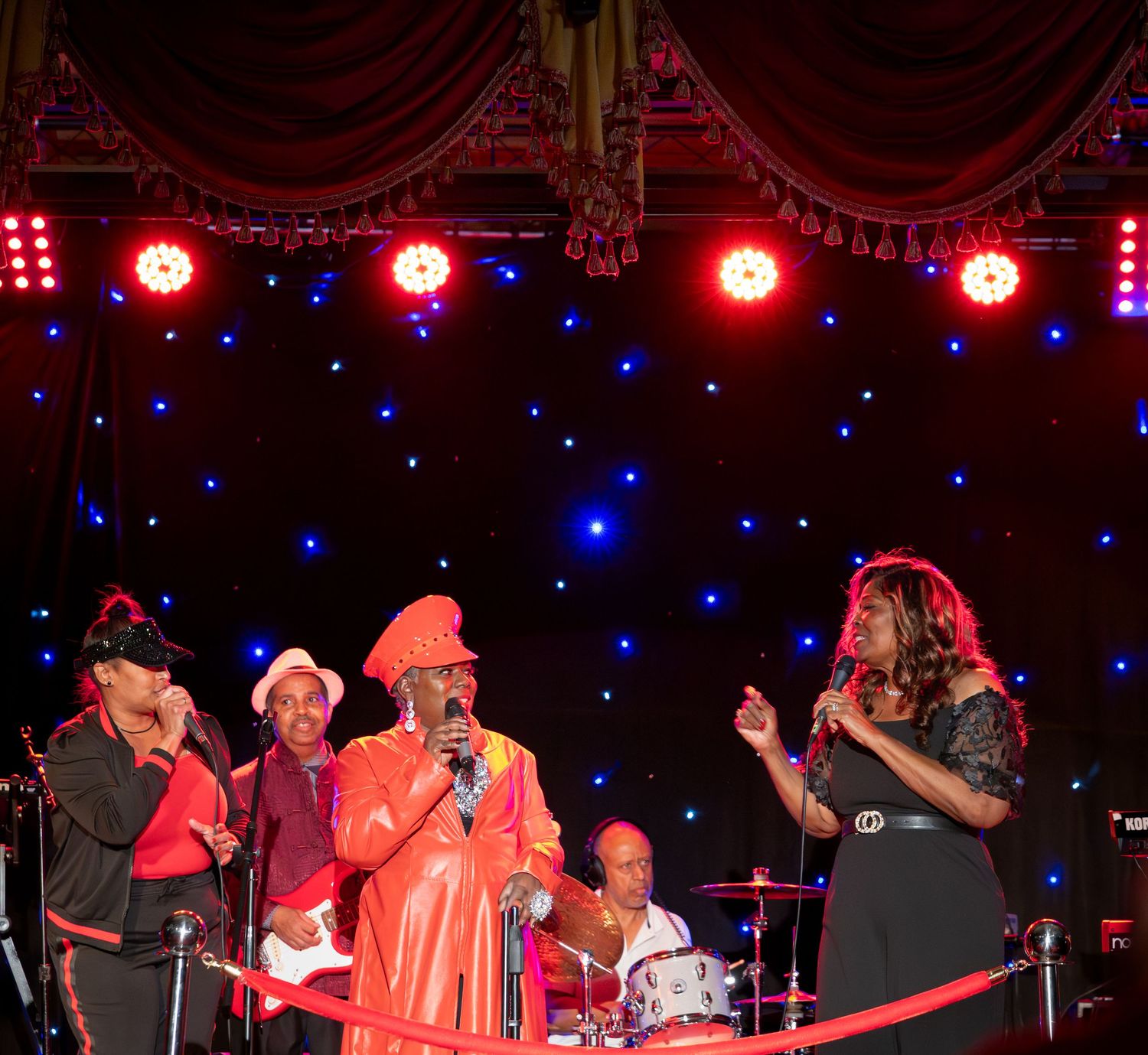 Band performs on stage with red spotlights and blue starlit backdrop creating dramatic ambiance.