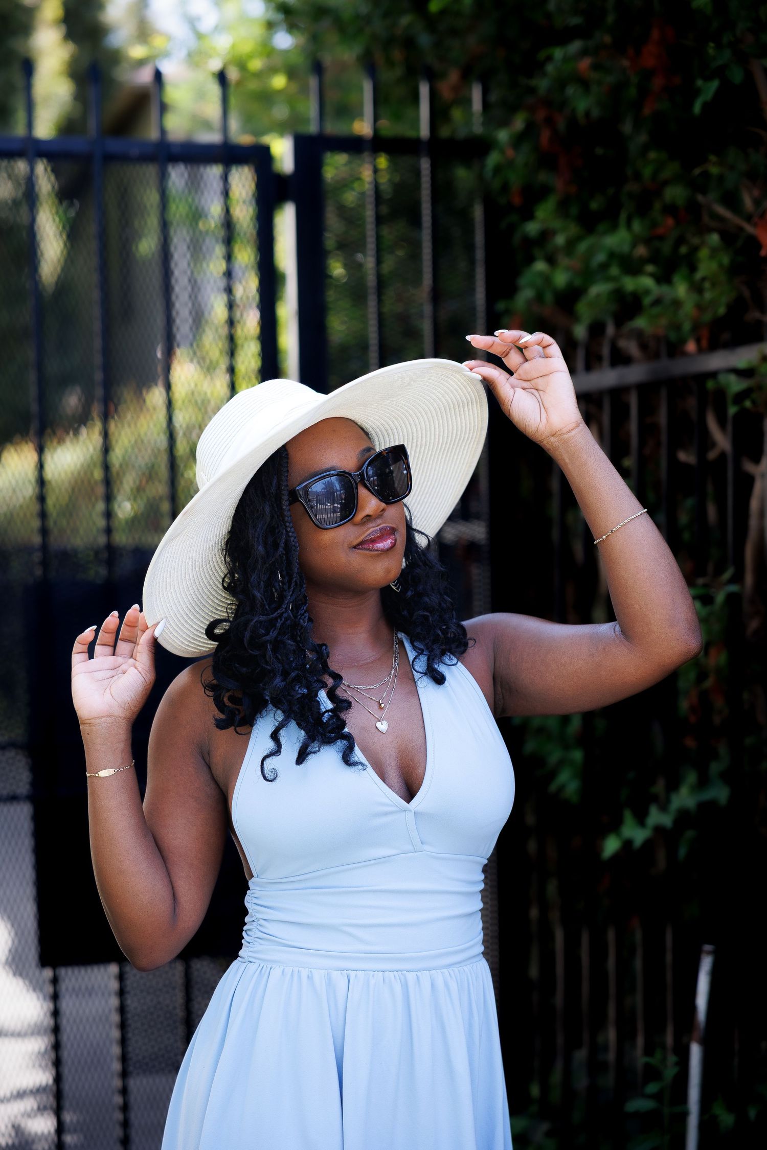 Person in a white dress and sunhat posing outdoors on a sunny day.