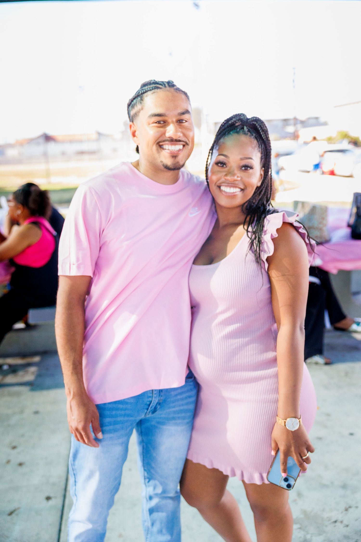Couple in coordinating pink outfits smiling together at outdoor event.