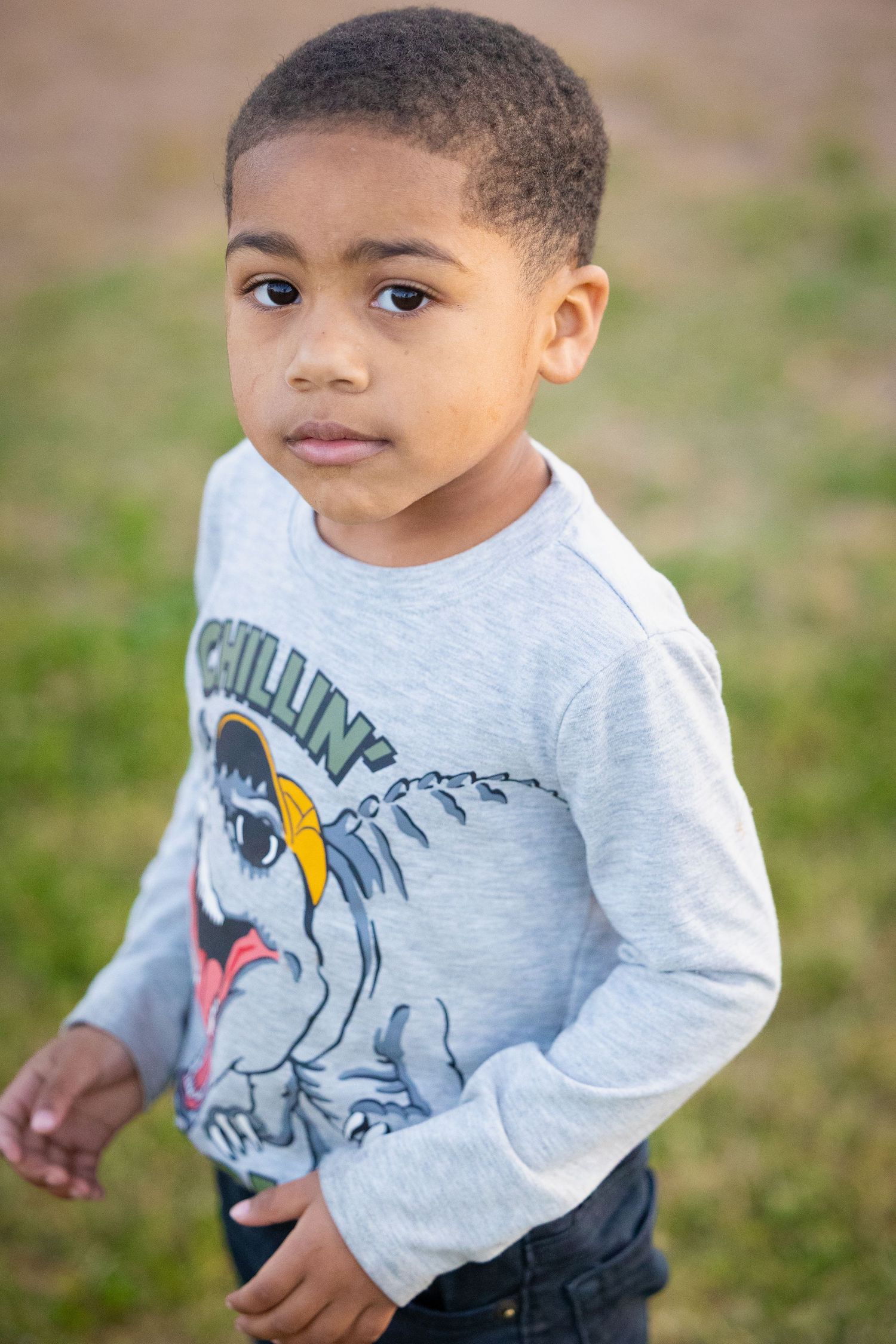 Child wearing gray sweatshirt with cartoon dinosaur graphic design.